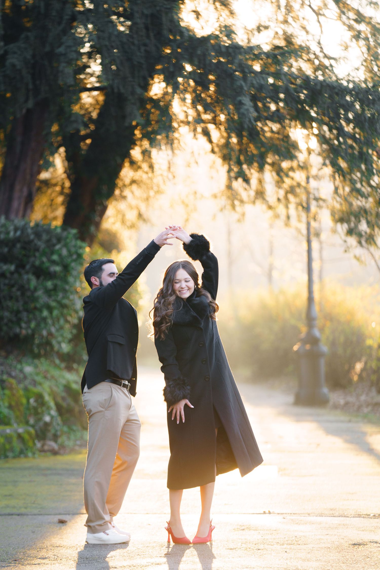A couple dancing together on a misty path at sunset with golden light filtering through trees in the background.