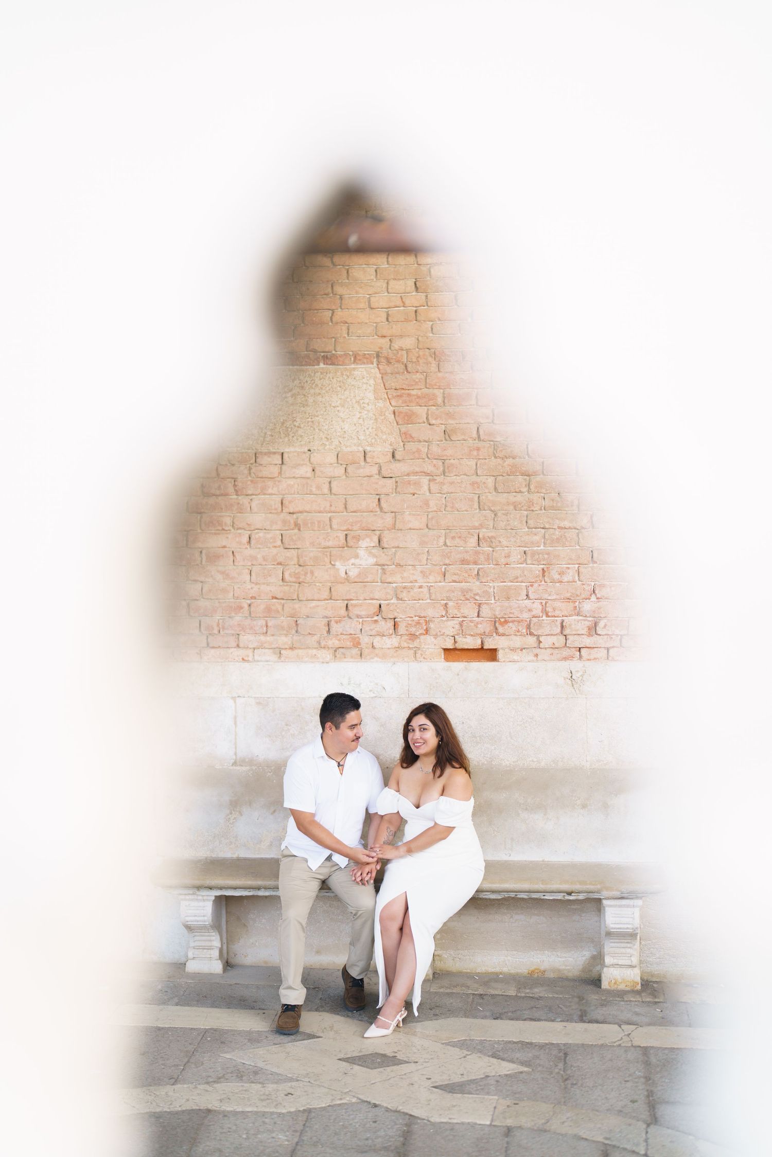 A couple in white outfits sits on stone steps together in a romantic outdoor setting.