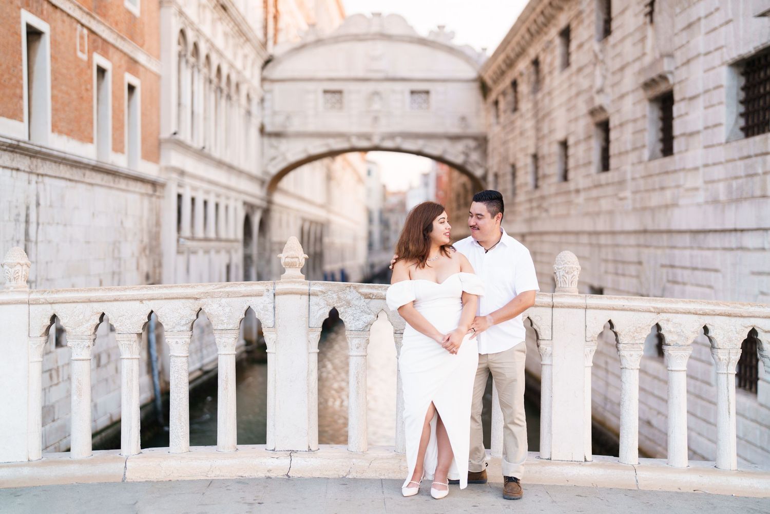 A romantic couple in white outfits embraces on the Bridge of Sighs in Venice, Italy.