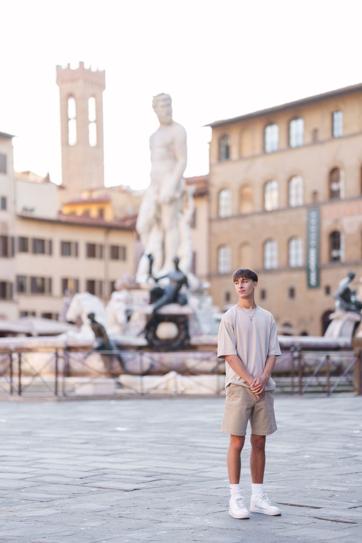 Person in casual attire stands in historic Italian plaza with Renaissance architecture and sculptures in background.