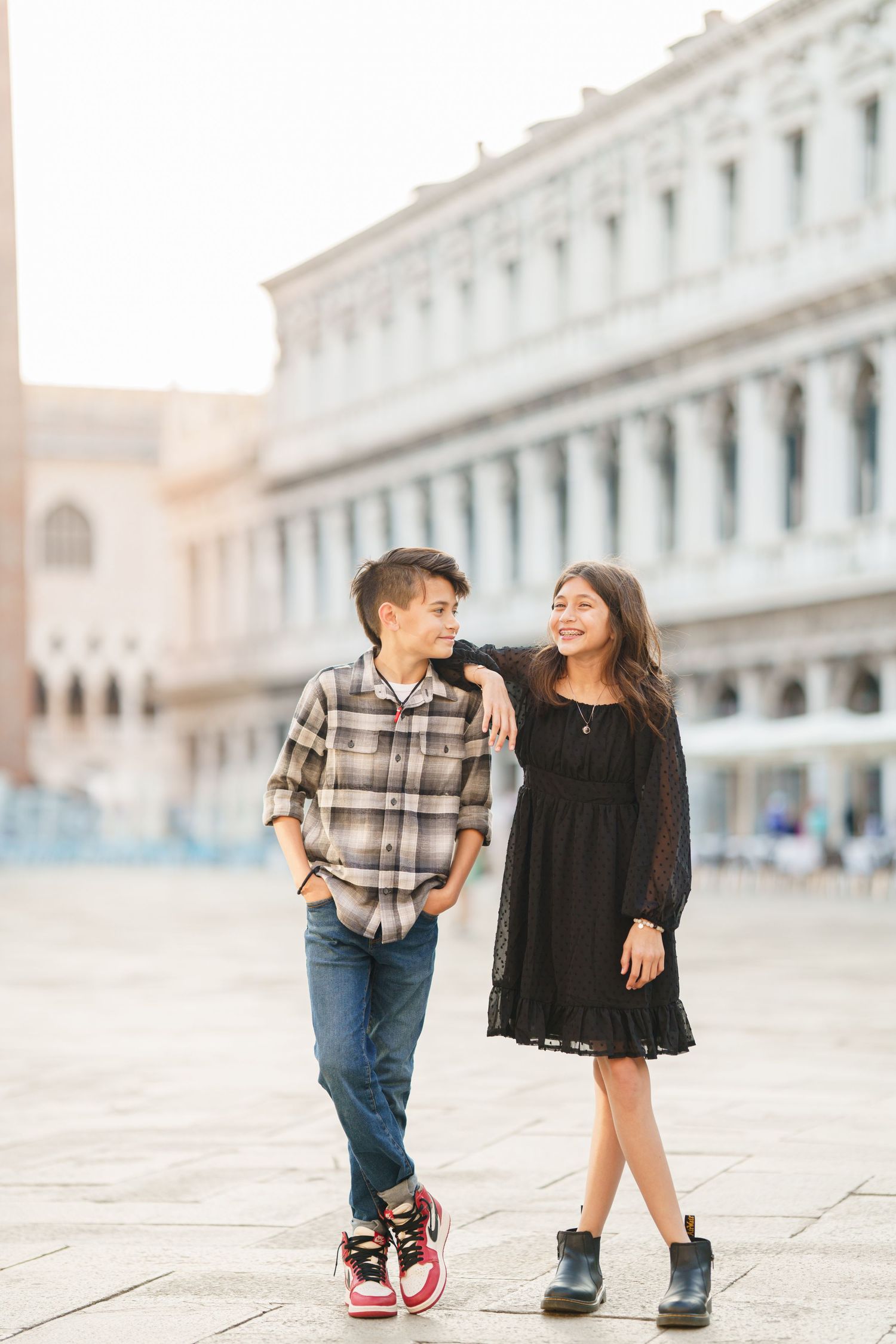 photographer veniceTwo children in casual outfits playfully interact on a historic European plaza with classic architecture in background.