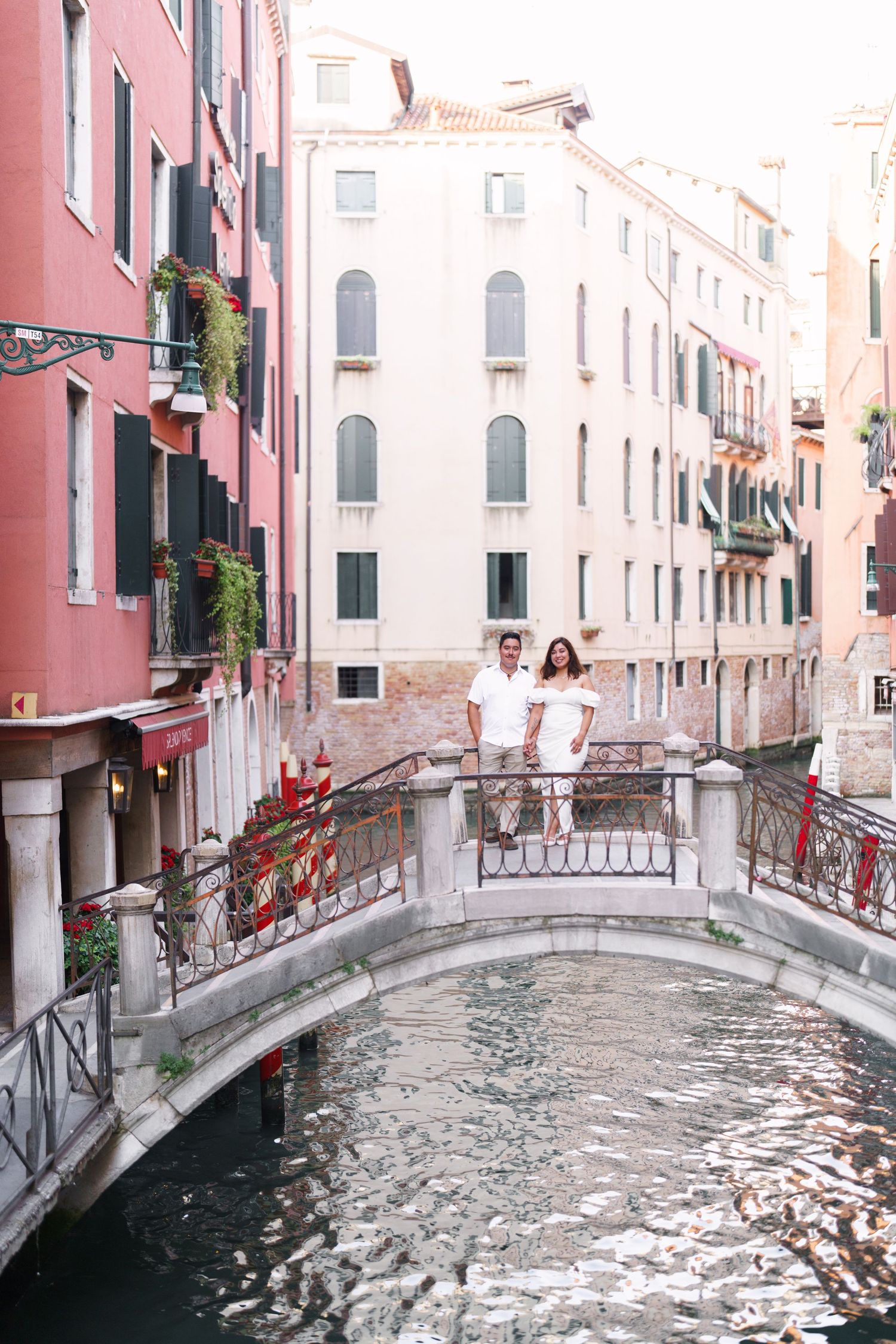 A series of small stone bridges cross over a narrow Venice canal between pink and white buildings with ornate architecture.