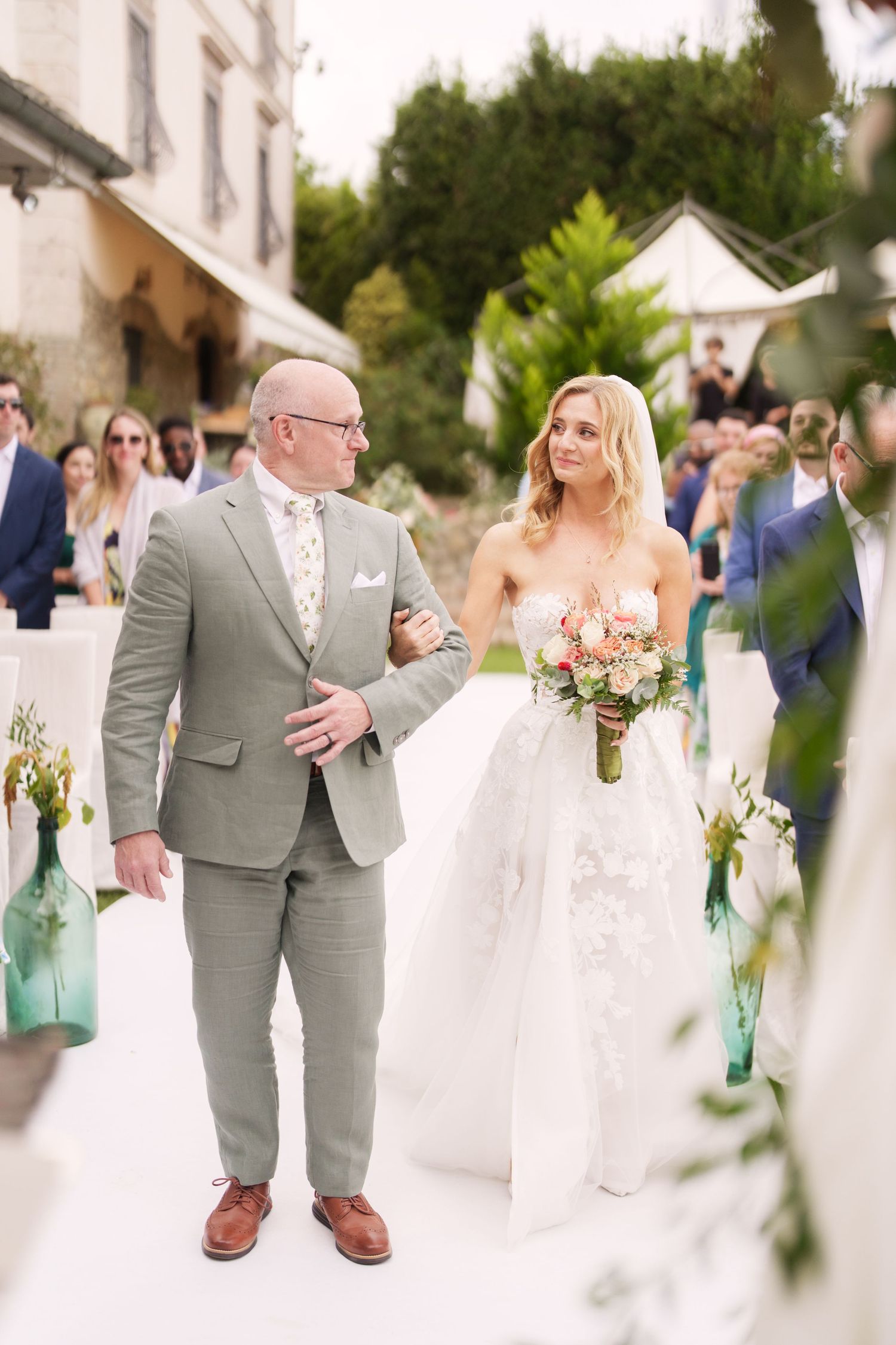 A wedding ceremony processional on a white aisle runner with blue glass bottle decorations.