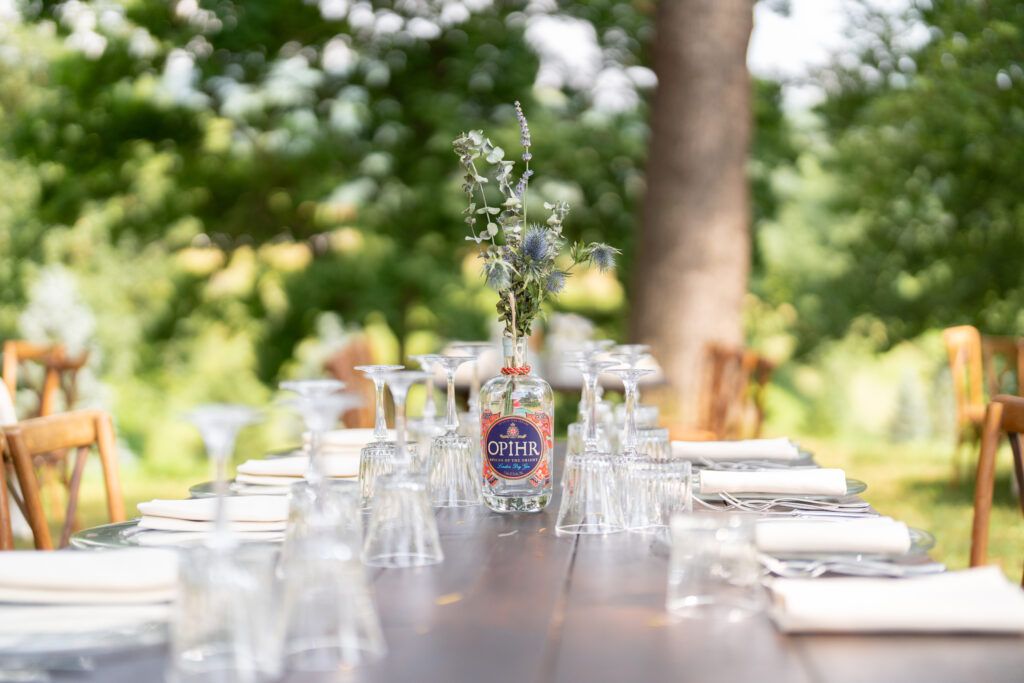 Long banquet tables set with glassware and place settings under natural outdoor lighting.