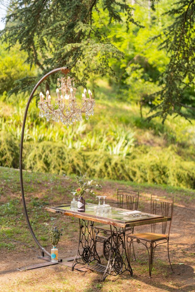 Rustic outdoor table settings with vintage sewing machine bases and elegant chandeliers in a garden setting.