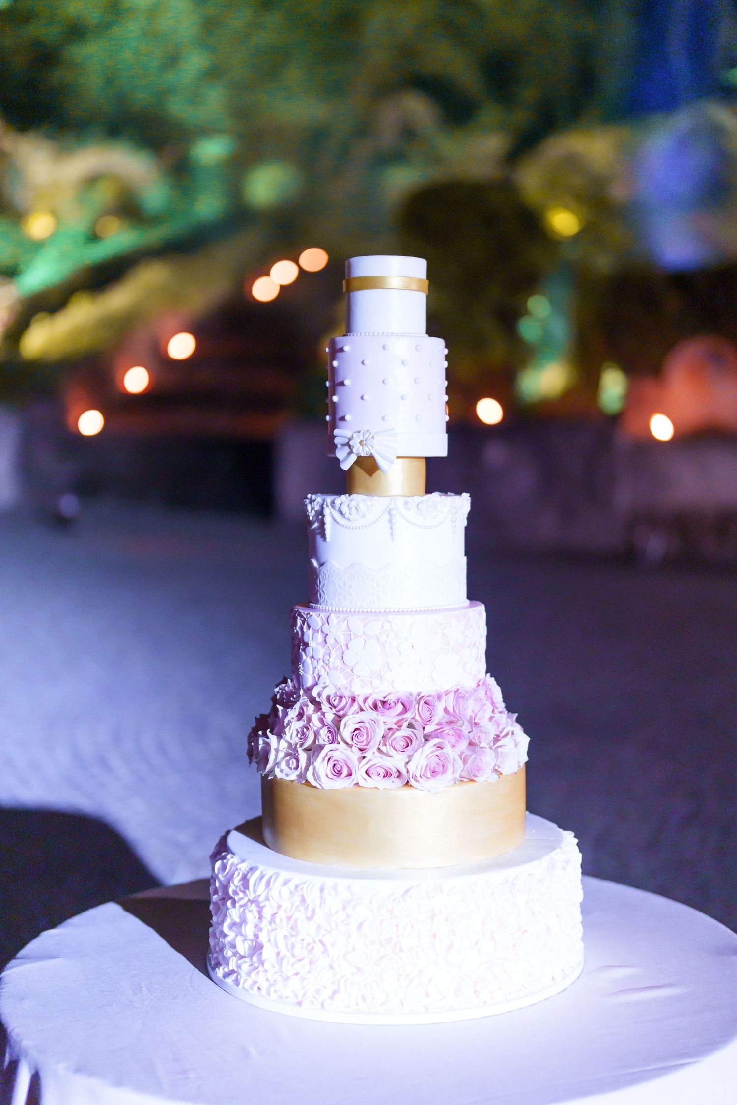 Elegant white wedding cake with delicate pink rose details and gold ribbon accents.