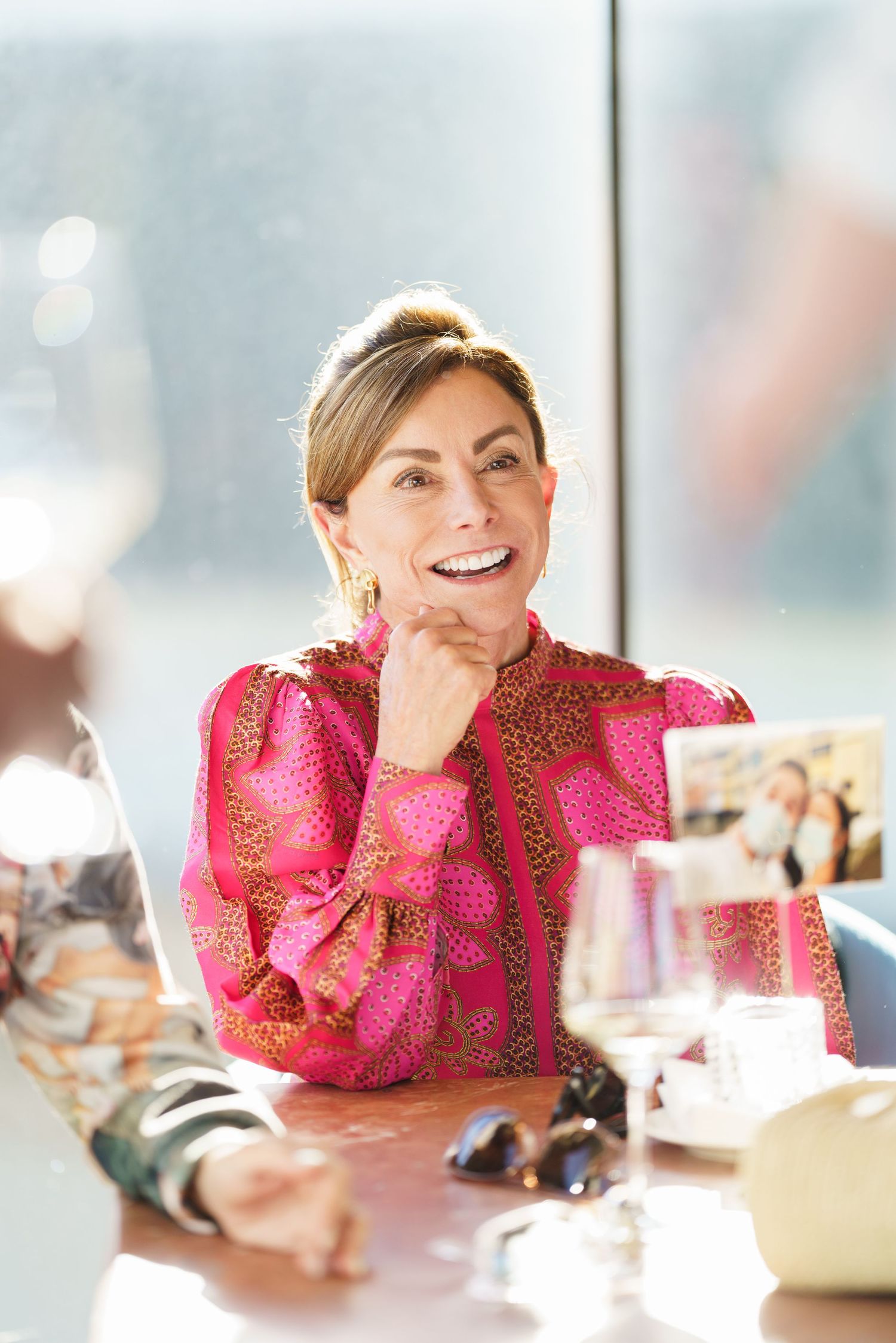 Person in bright pink ruffled top sitting at table with hand on chin.