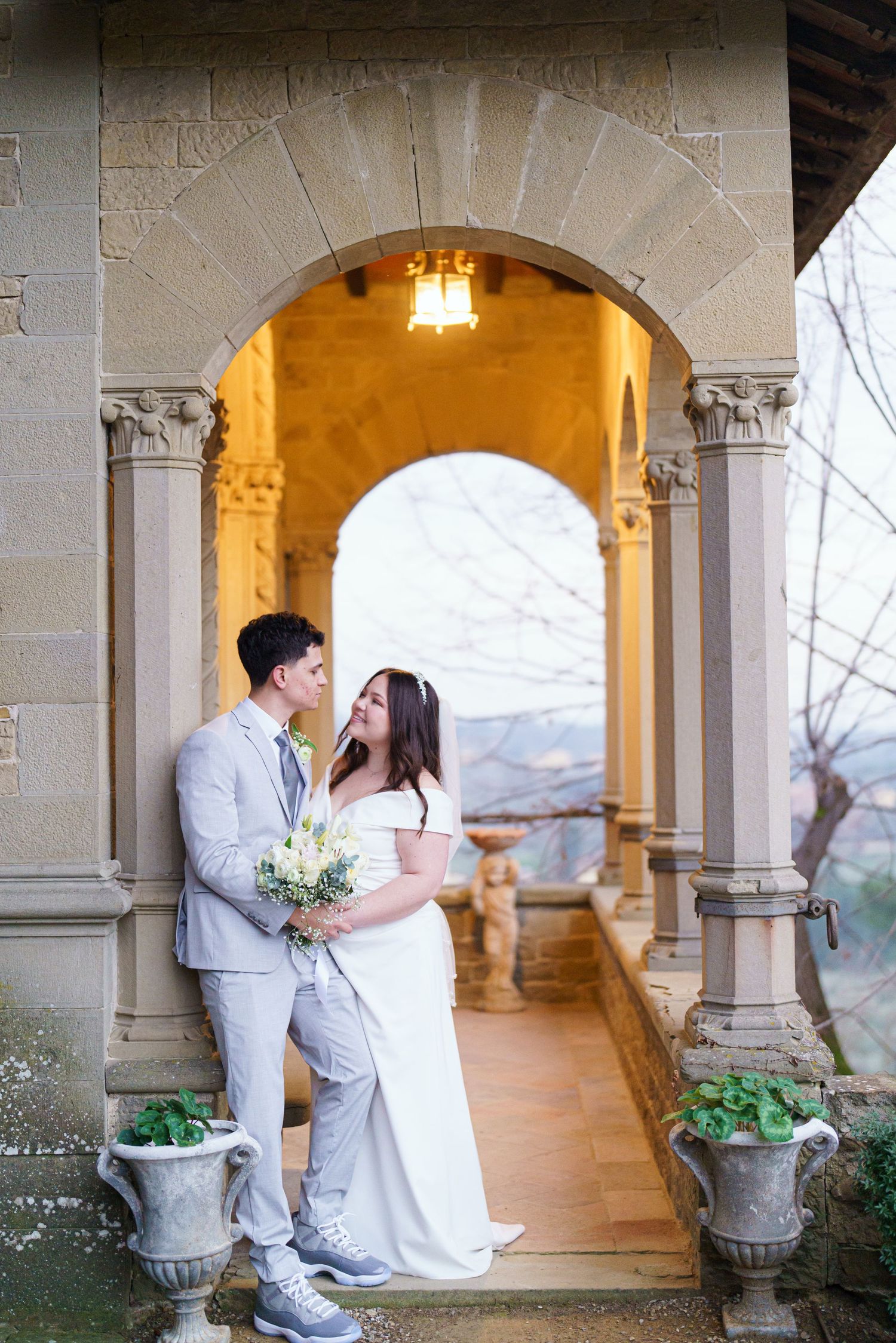 Romantic wedding portraits under stone archways with warm lighting and mountain backdrop.