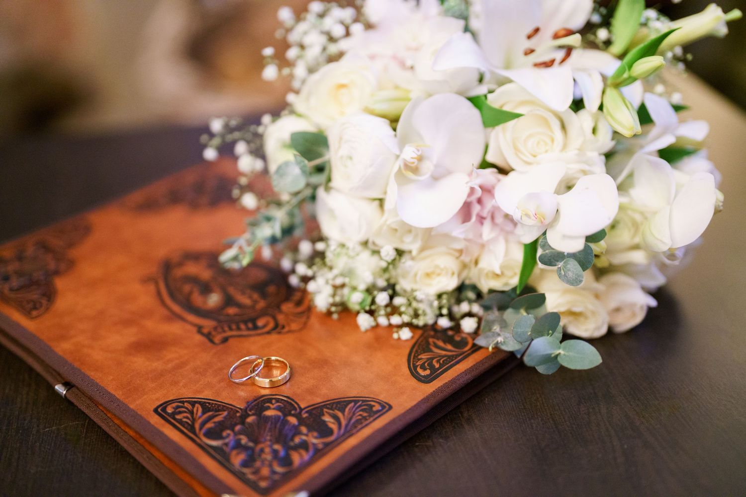 White floral bouquet with roses and greenery displayed on an ornate wooden surface.