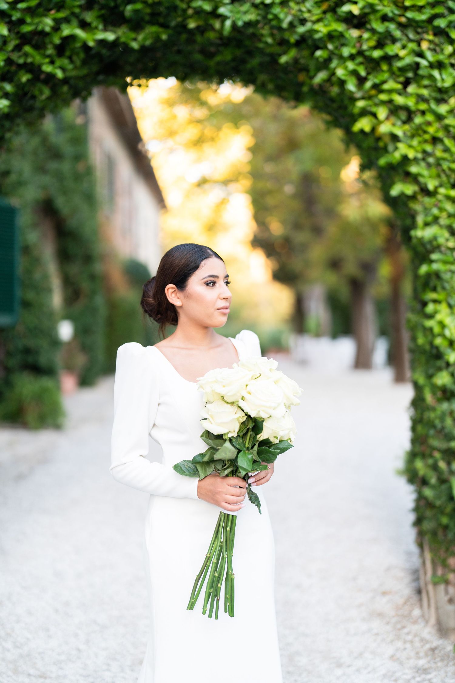 Elegant bridal portrait with white roses under ivy-covered archway.