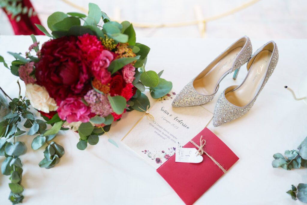 Wedding details including red florals, invitation suite, and bridal shoes.