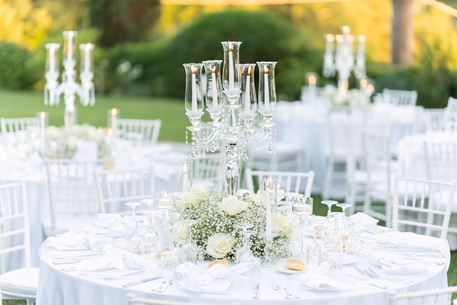 Elegant outdoor wedding reception table setting with crystal candelabras and white floral centerpieces.