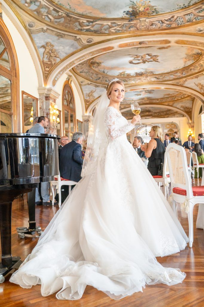 Elegant wedding gown with flowing train twirls on ornate ballroom floor with gilded ceiling and chandeliers.