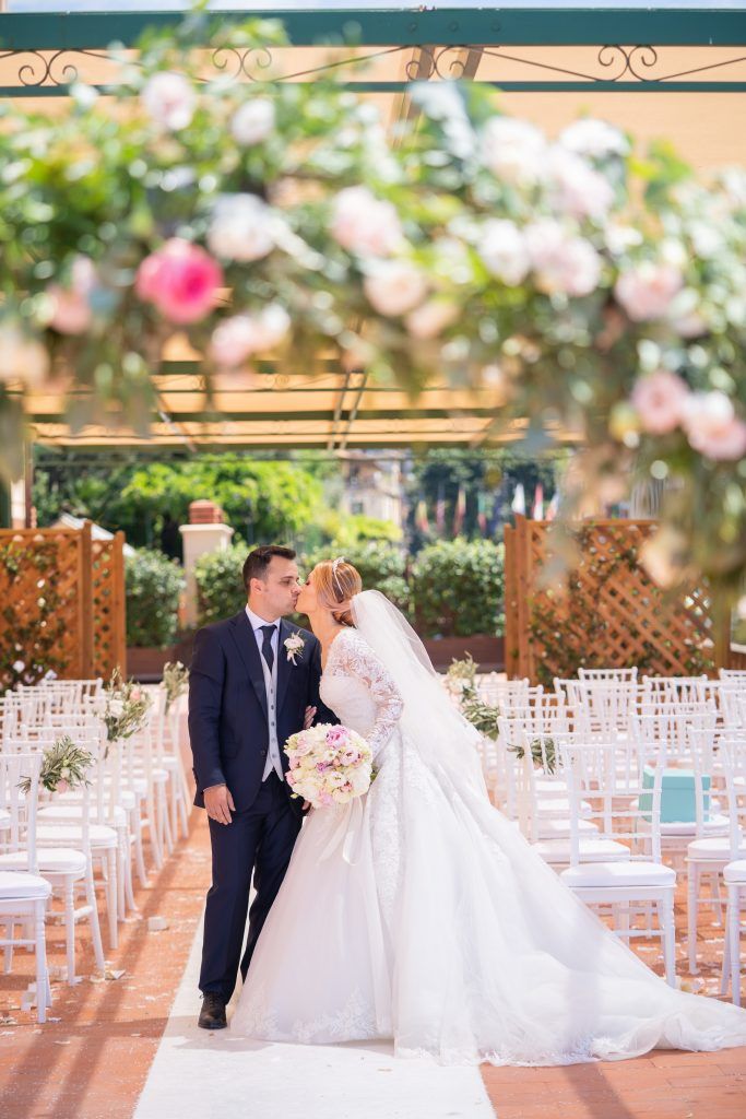 A romantic wedding ceremony setup with white chairs and pink floral decorations in an elegant outdoor venue.