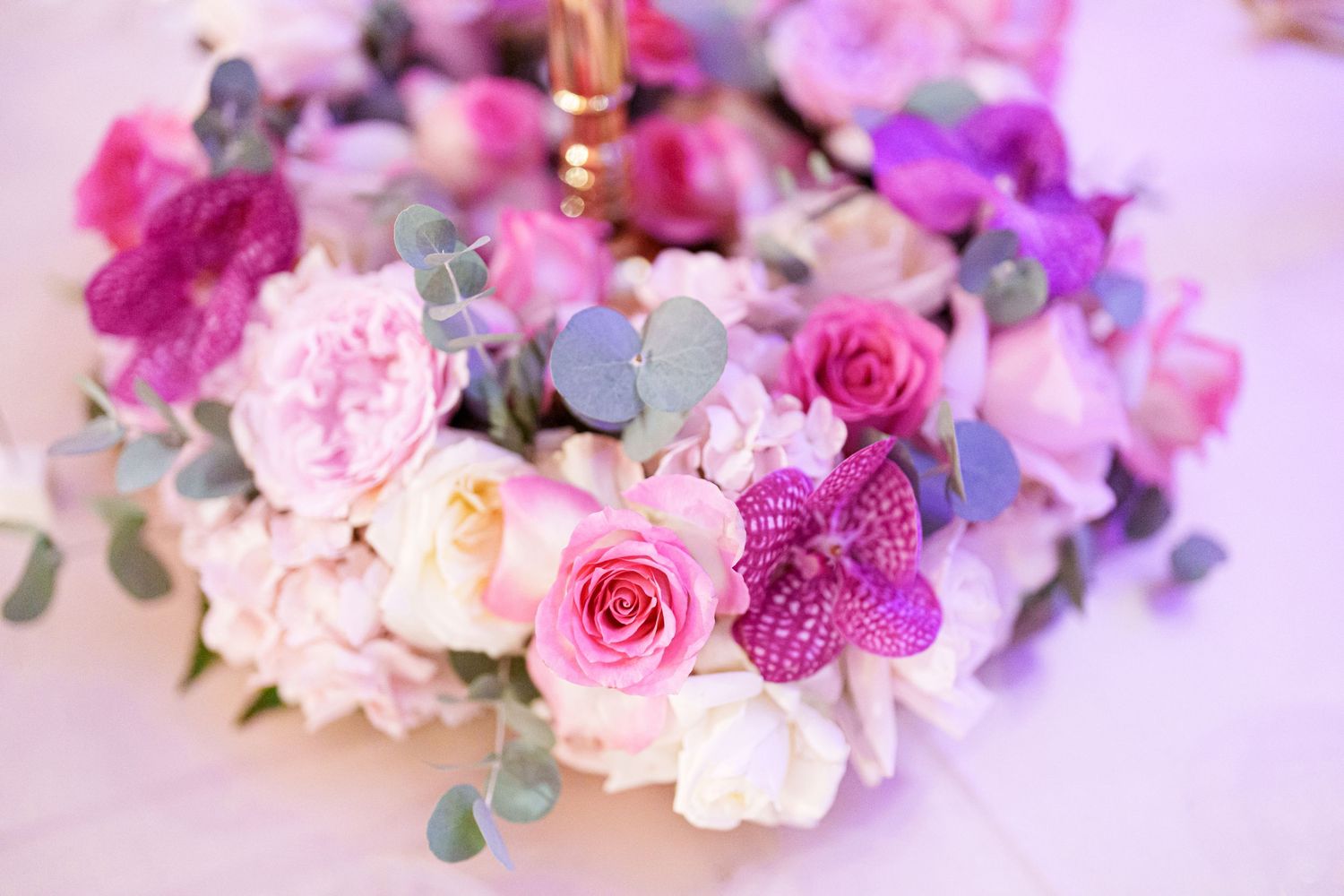 Pink and purple floral arrangement with roses and orchids for wedding centerpiece.
