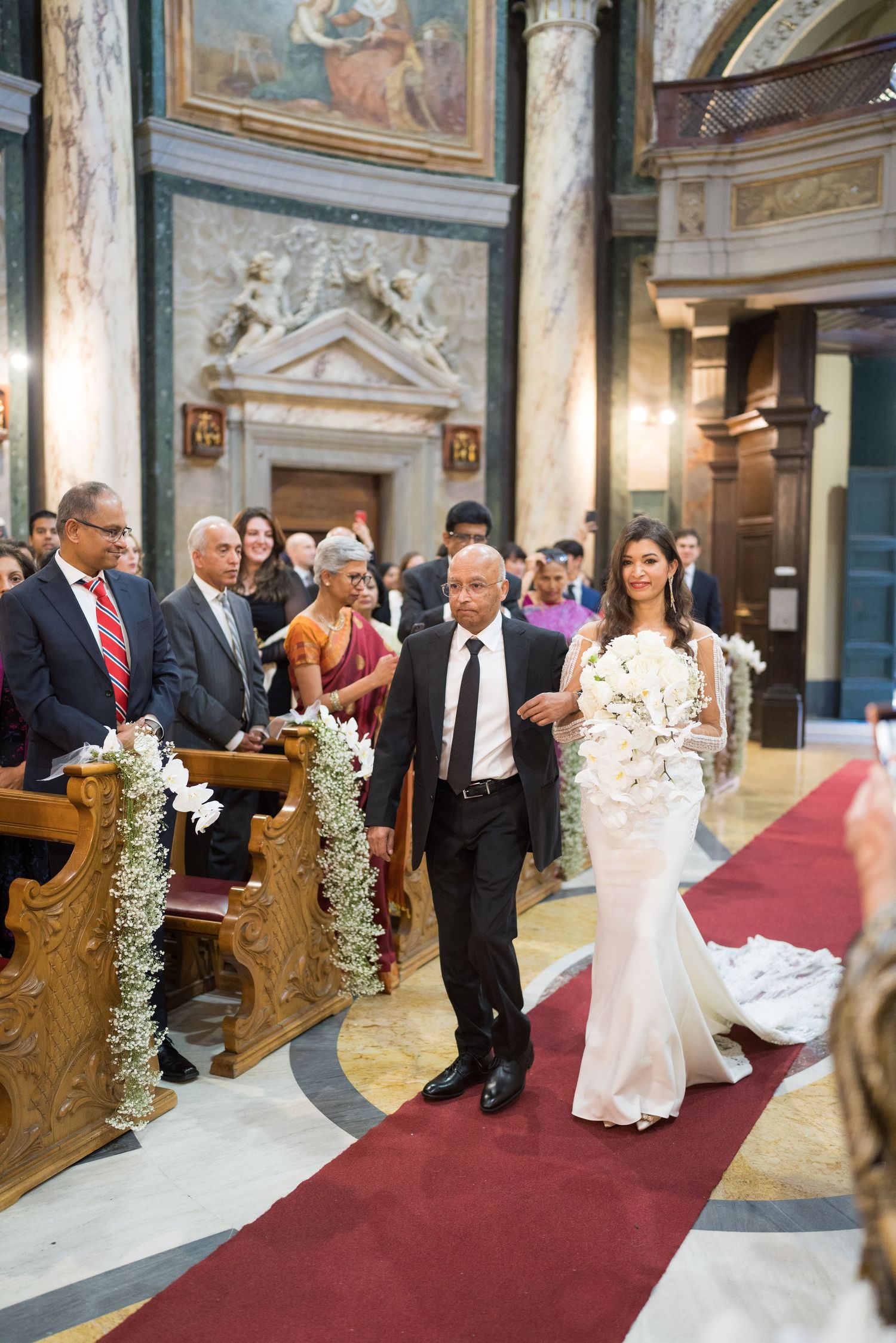A wedding ceremony procession in an ornate church with marble columns and religious artwork.