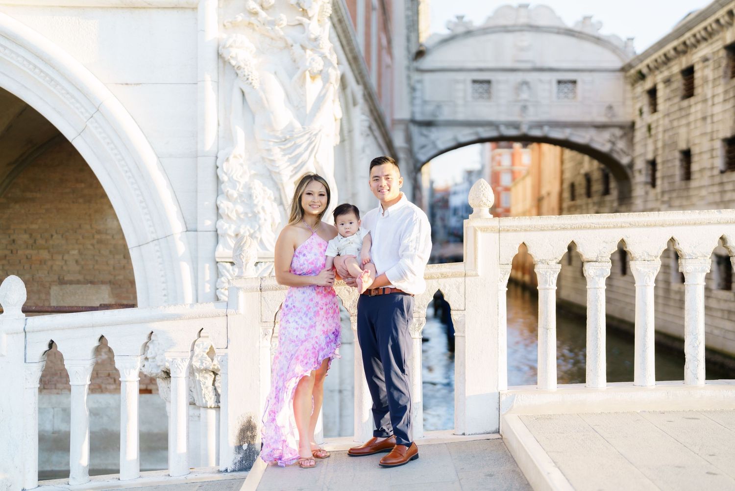 Family of three posing on a Venice bridge near the Bridge of Sighs on a sunny day.