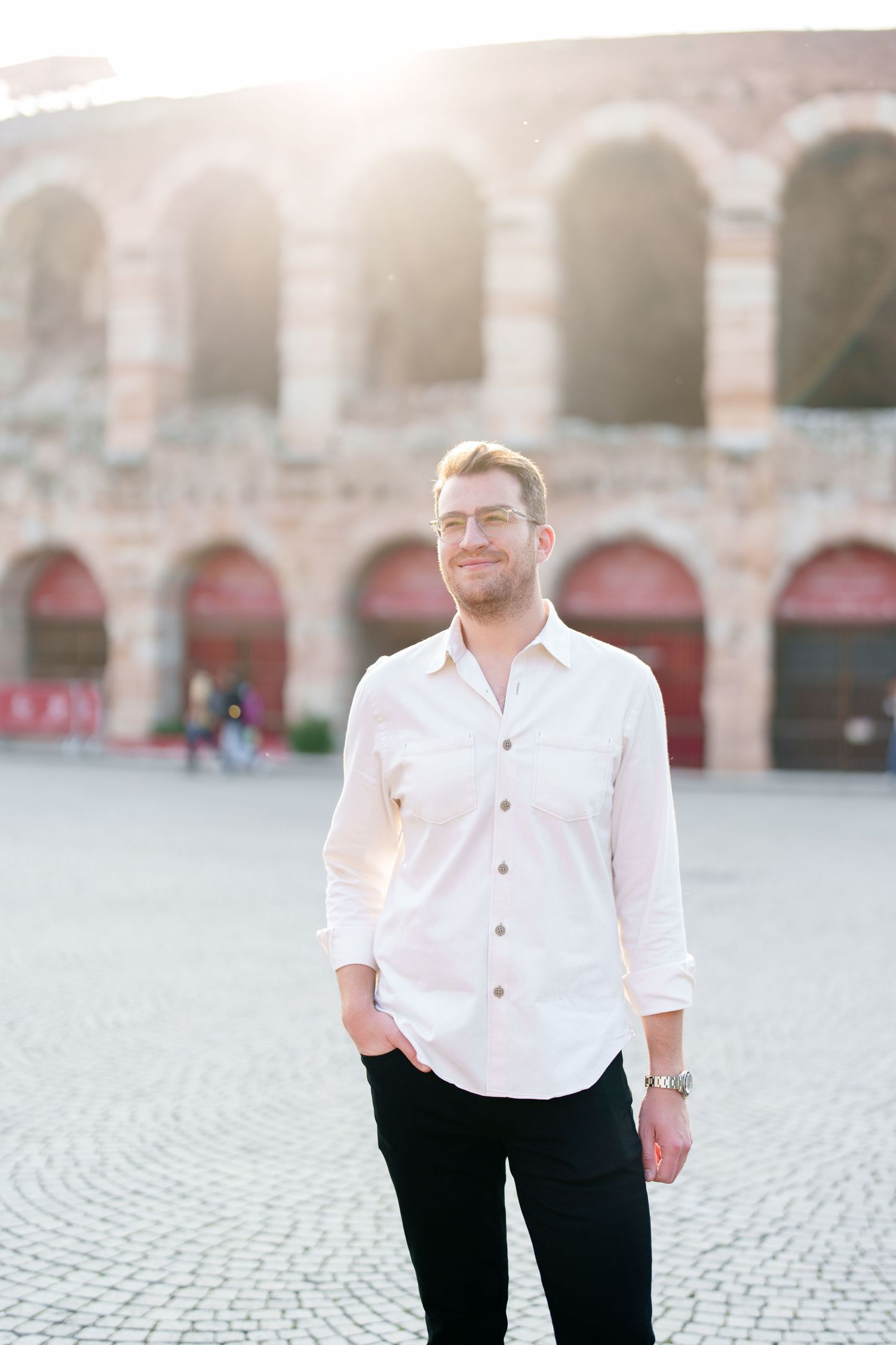 A series of four similar photos showing someone in a white button-down shirt and black pants standing in front of stone arches.
