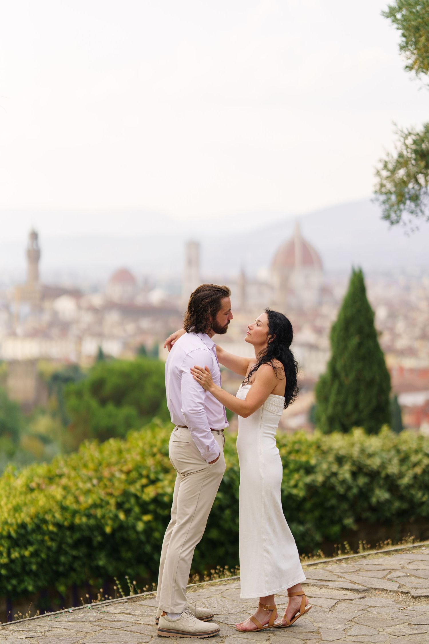 Romantic couple embraces on a hilltop overlooking Florence, Italy with the iconic Duomo cathedral visible in the background.