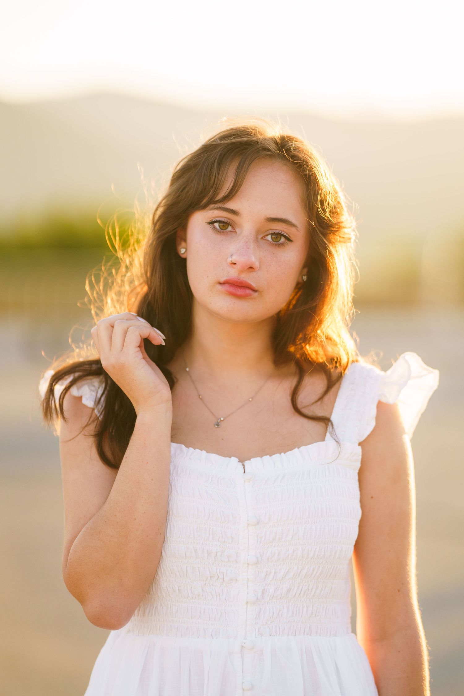 A young girl in a white sundress poses outdoors during golden hour with sunlit hair.