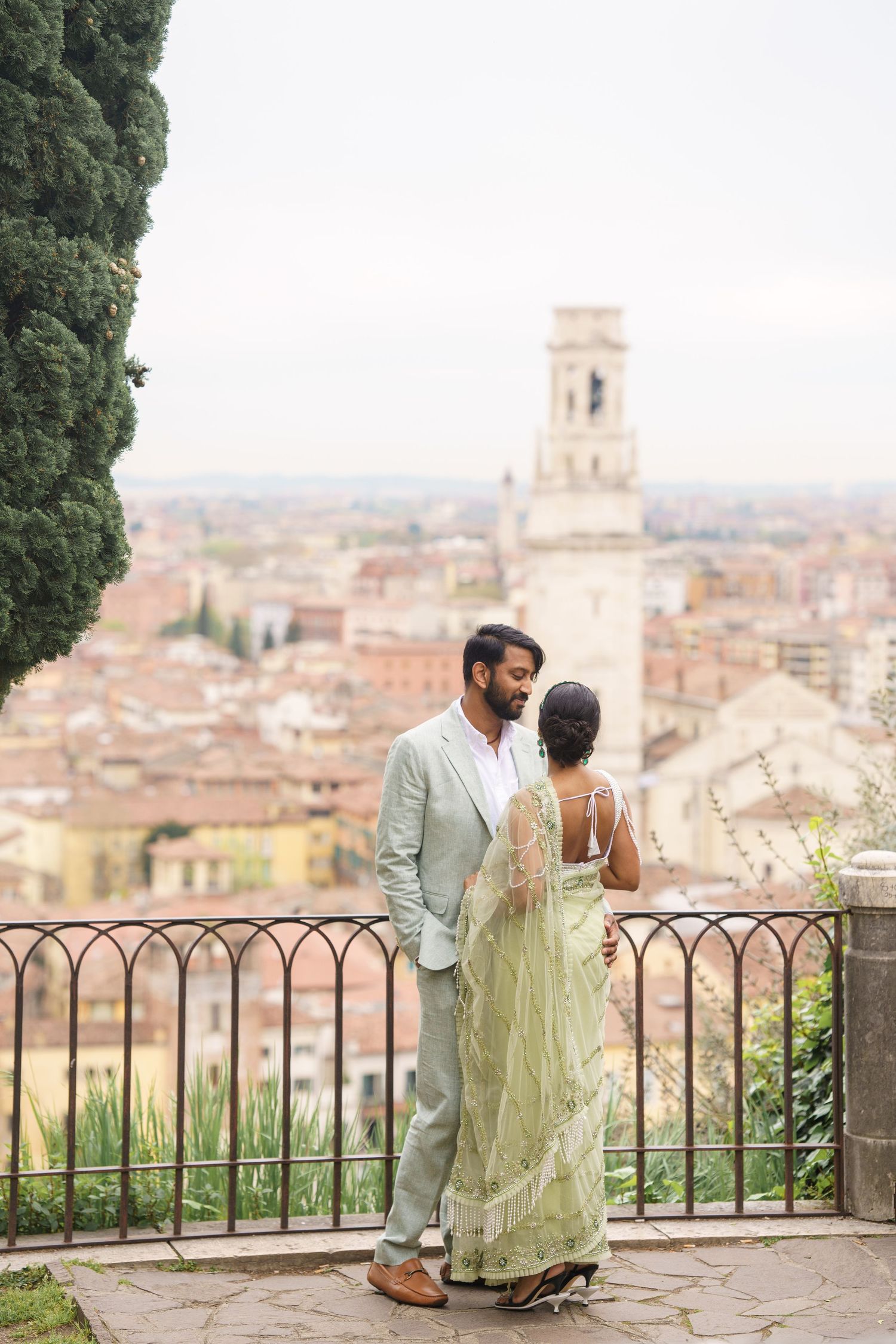 A couple shares a romantic moment overlooking a scenic Italian cityscape with terracotta roofs and church towers.