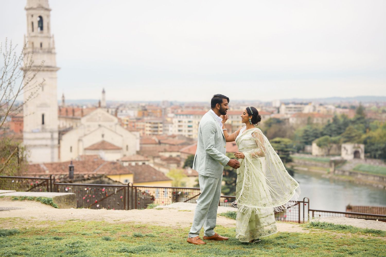A couple in traditional Indian attire dances together on a scenic overlook of Florence, Italy with historic architecture visible.