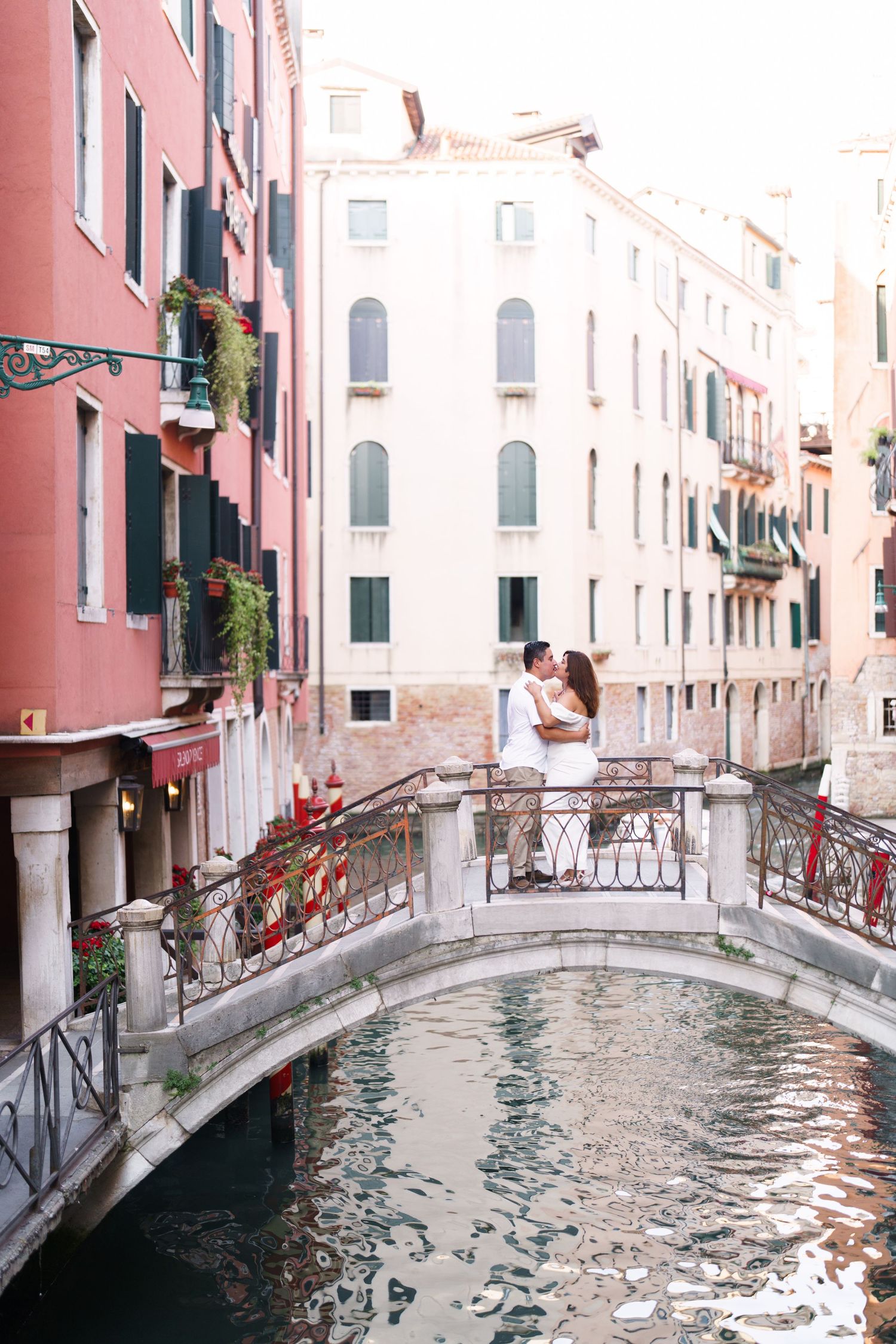 A scenic view of a small bridge over a Venetian canal with pink and white buildings in the background.