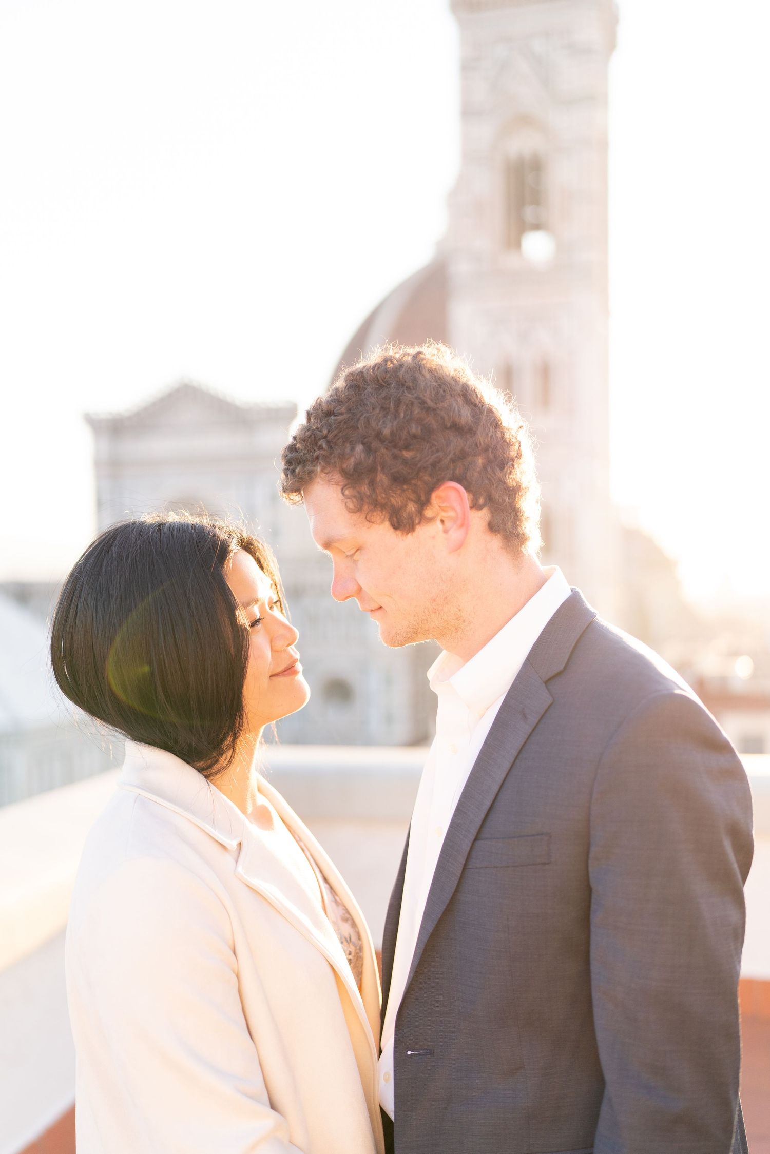 A couple shares an intimate moment at sunset on a rooftop with a cityscape backdrop.