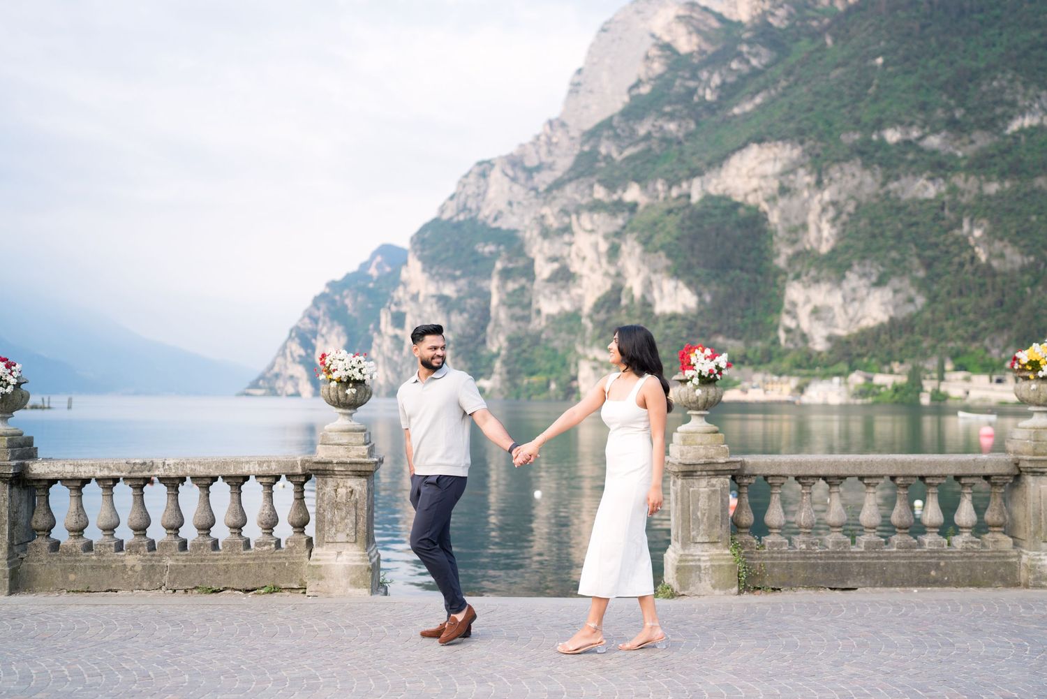 A scenic view of Lake Garda in Italy with mountains, boats, and people walking along the waterfront promenade.