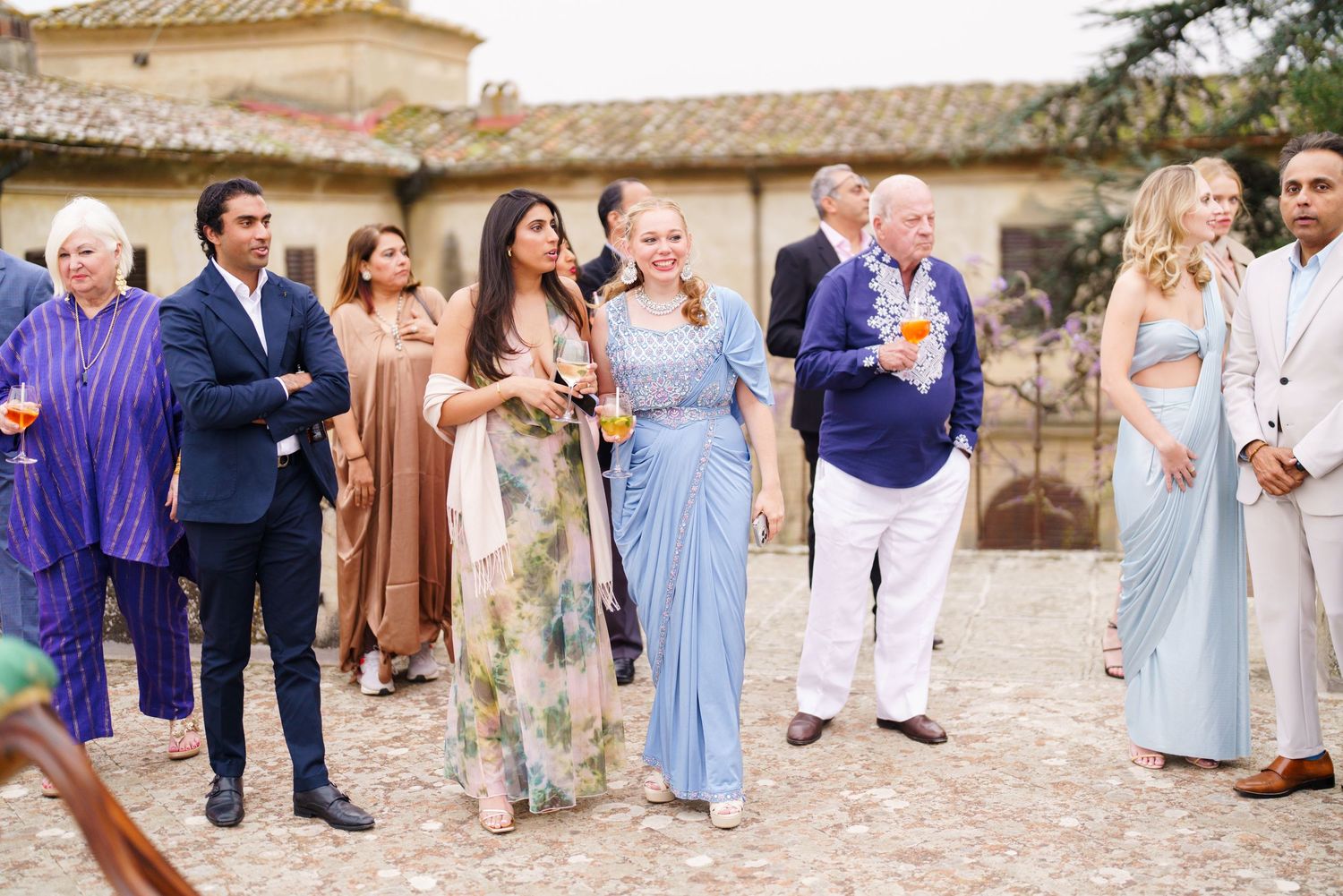 Wedding party and guests gathered for photos outside a Mediterranean style building.