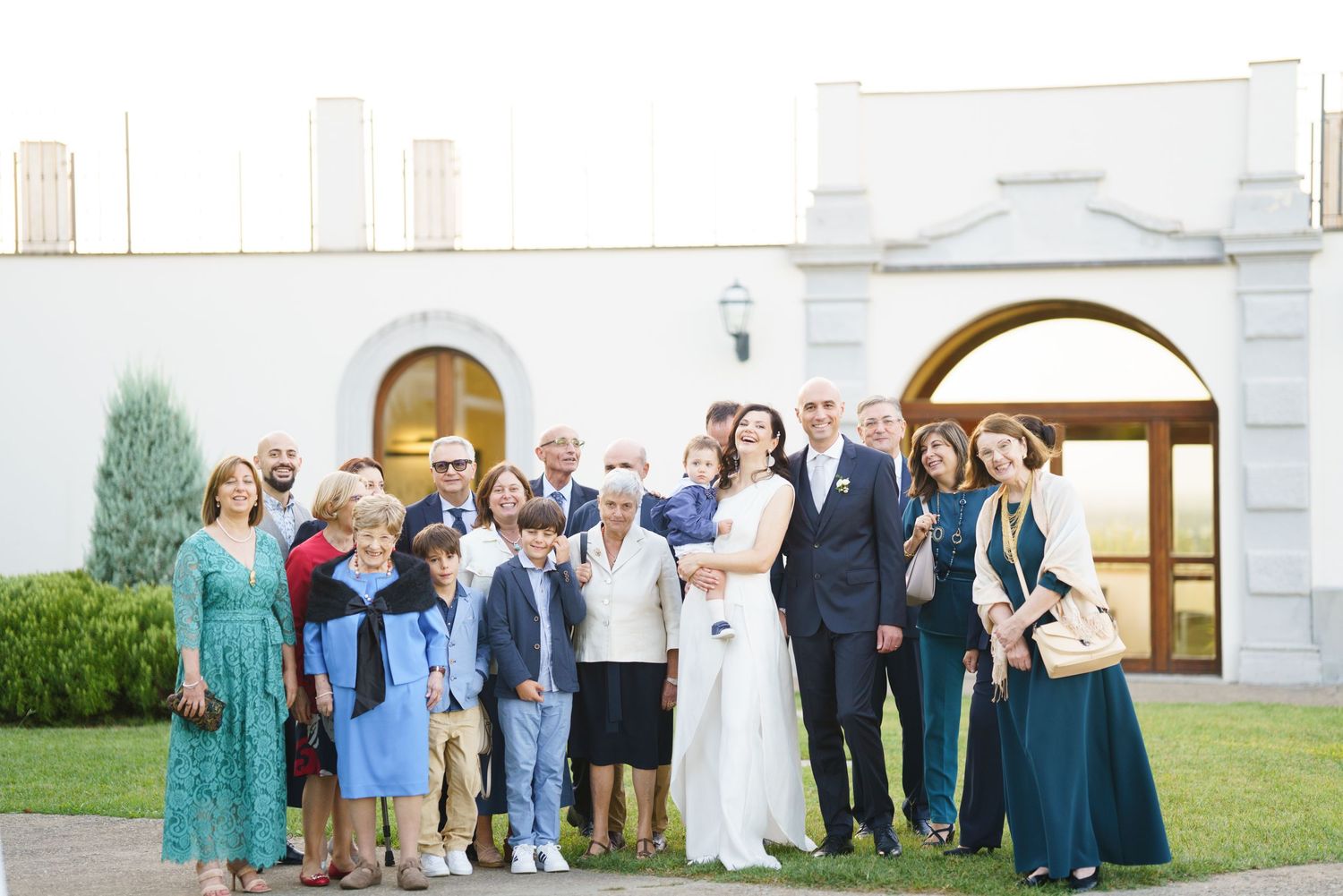 Wedding guests assembled on lawn in front of white church building for group photos.