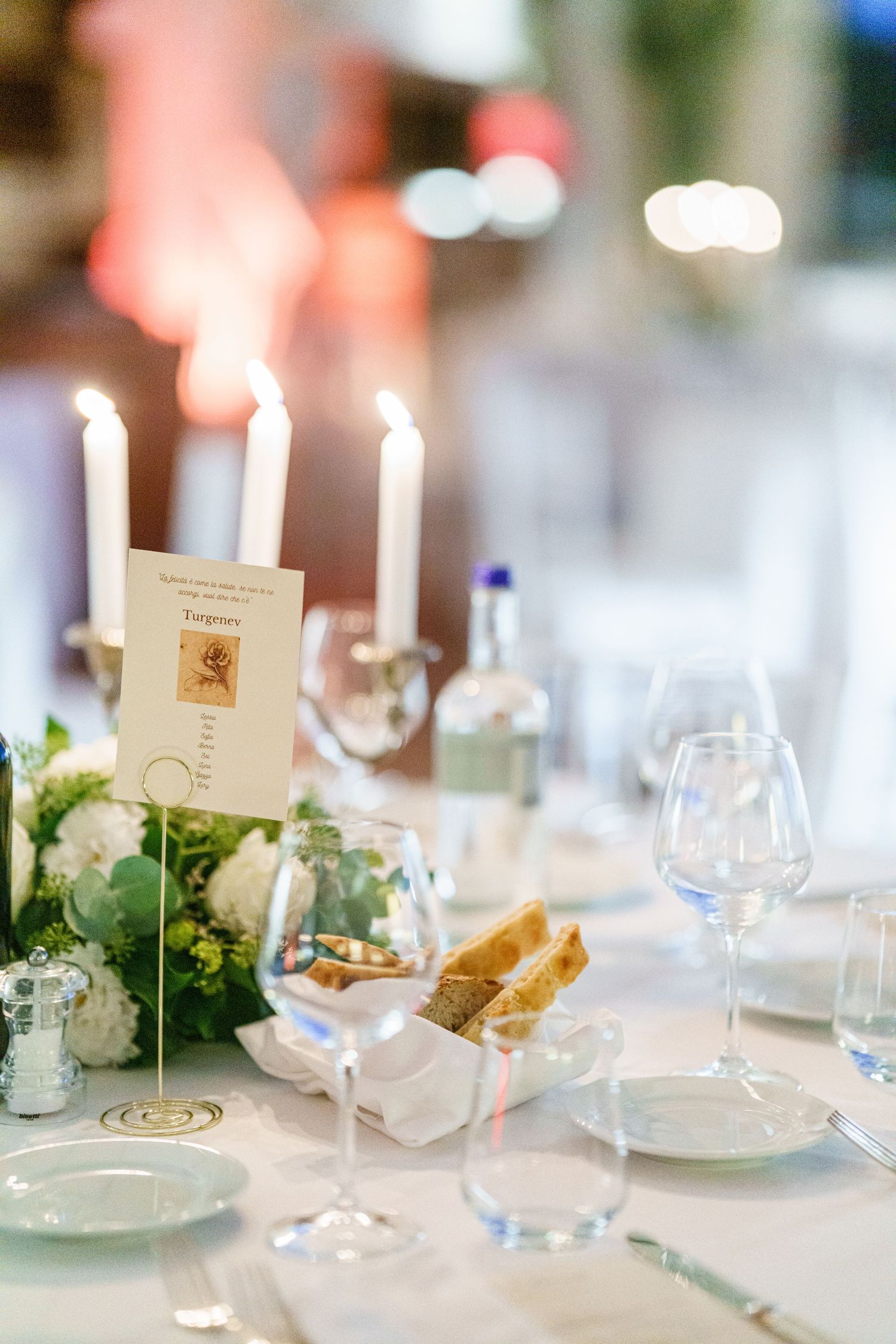 Close-up of wedding table settings with white candles, place cards, and greenery accents.
