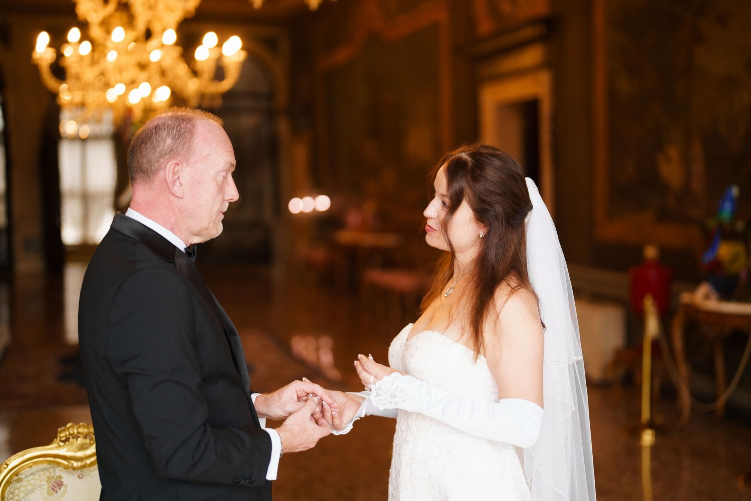 A couple shares their first dance at an elegant wedding reception with warm lighting and chandeliers overhead.