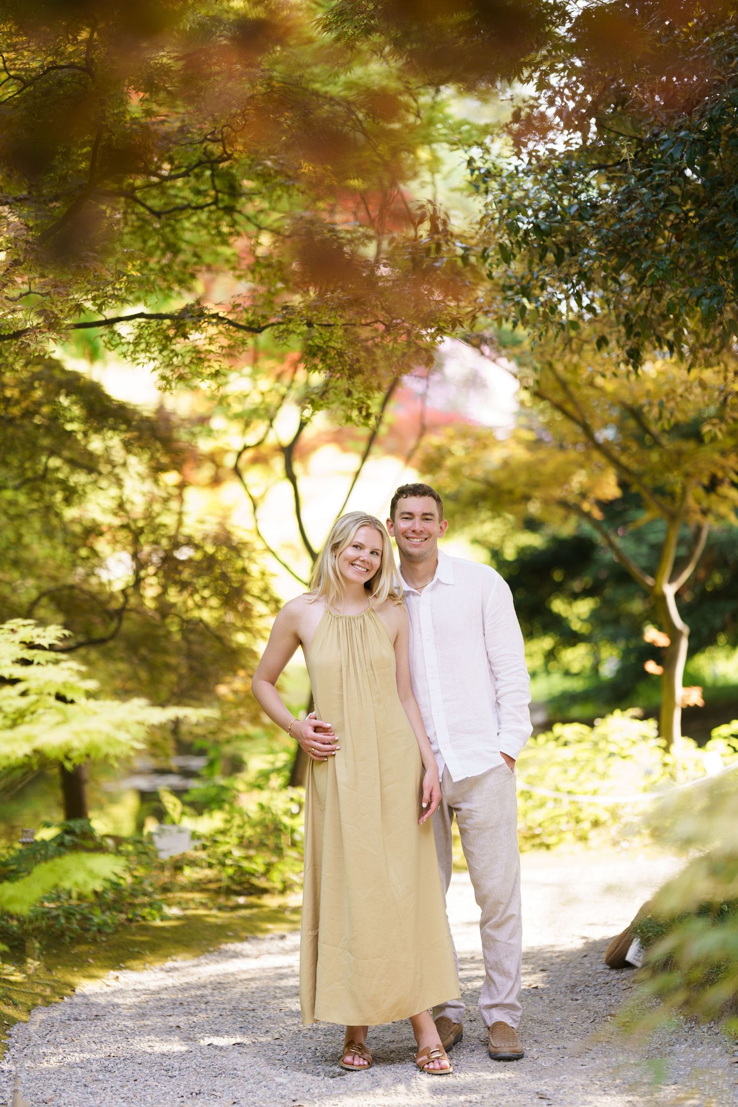 Smiling couple posing on a garden path surrounded by colorful autumn trees in a serene Japanese garden.