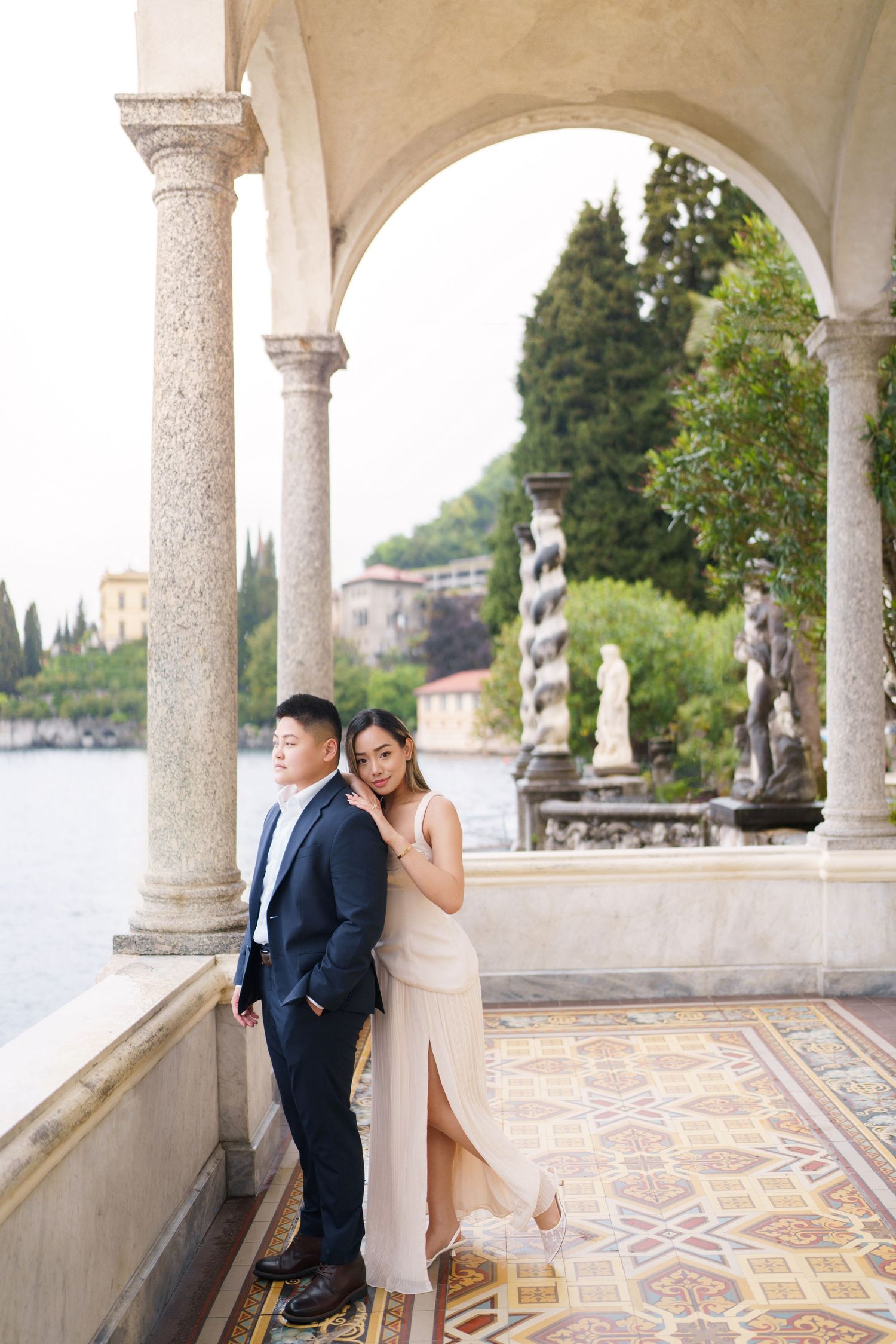 Elegant couple posing under ornate stone arches at Villa del Balbianello on Lake Como, Italy.