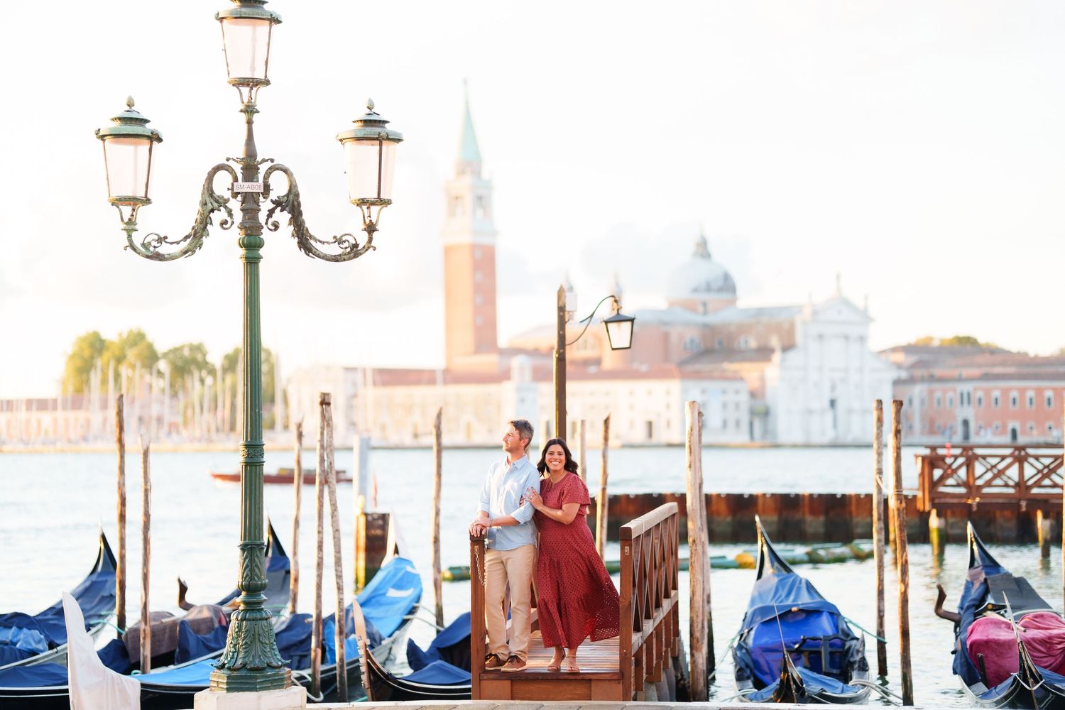 Couple standing on a dock in Venice, Italy, with gondolas and San Giorgio Maggiore island in the background.