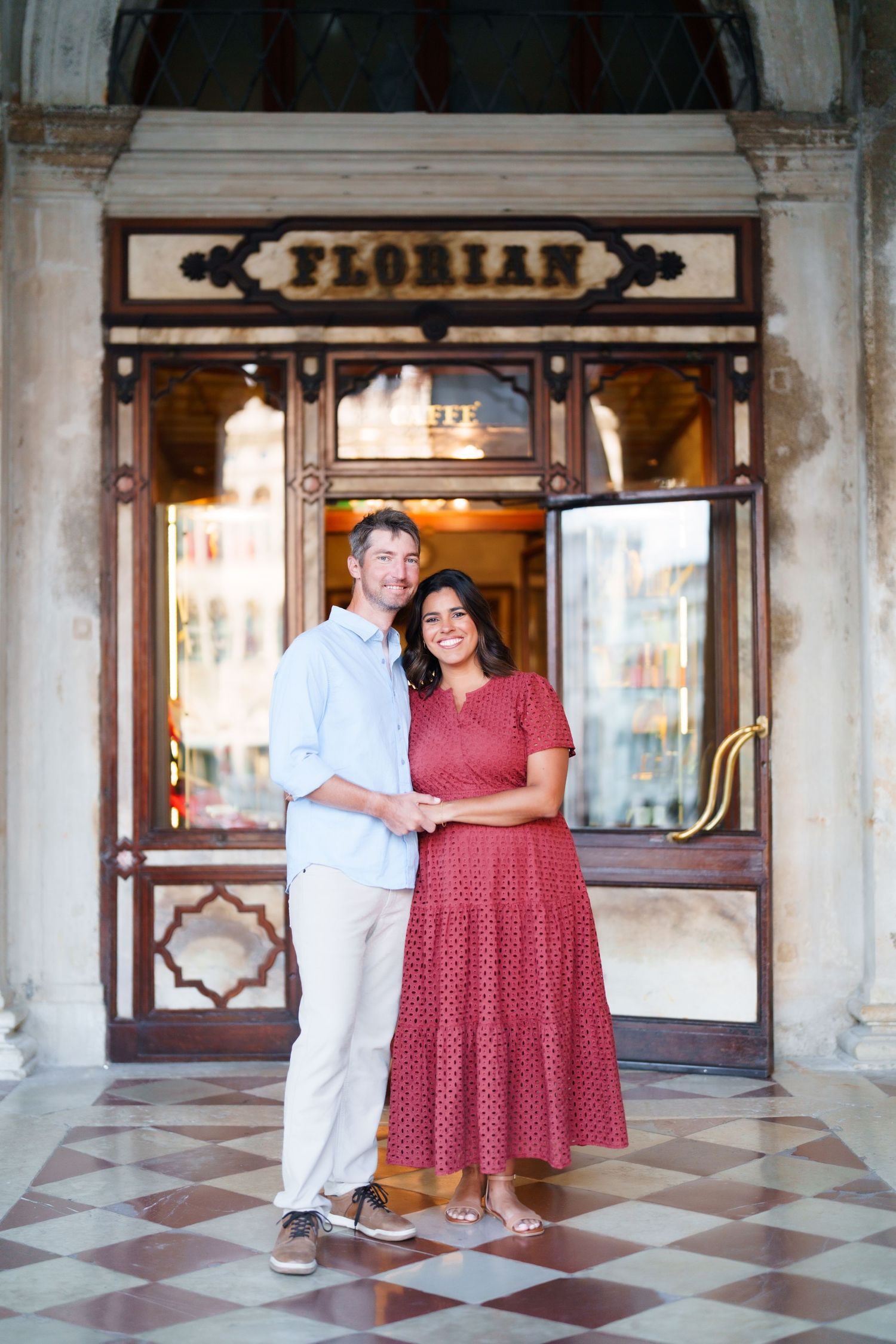 Couple smiling together outside Caffe Florian in Venice, Italy, woman in red dress, man in light blue shirt.