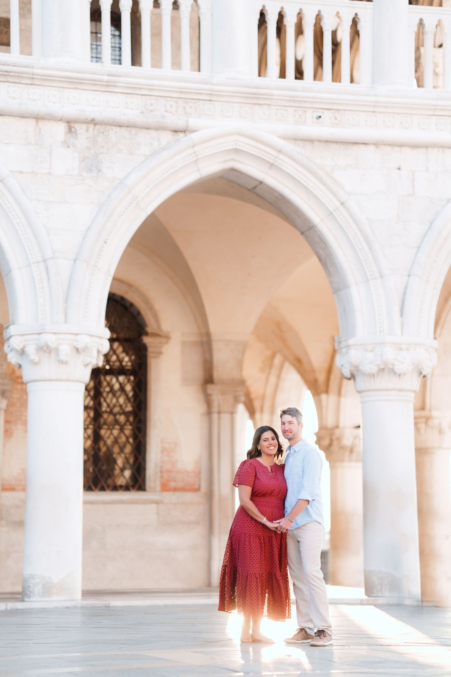 Couple embracing under ornate white Gothic arches of the Doge's Palace in Venice, Italy.