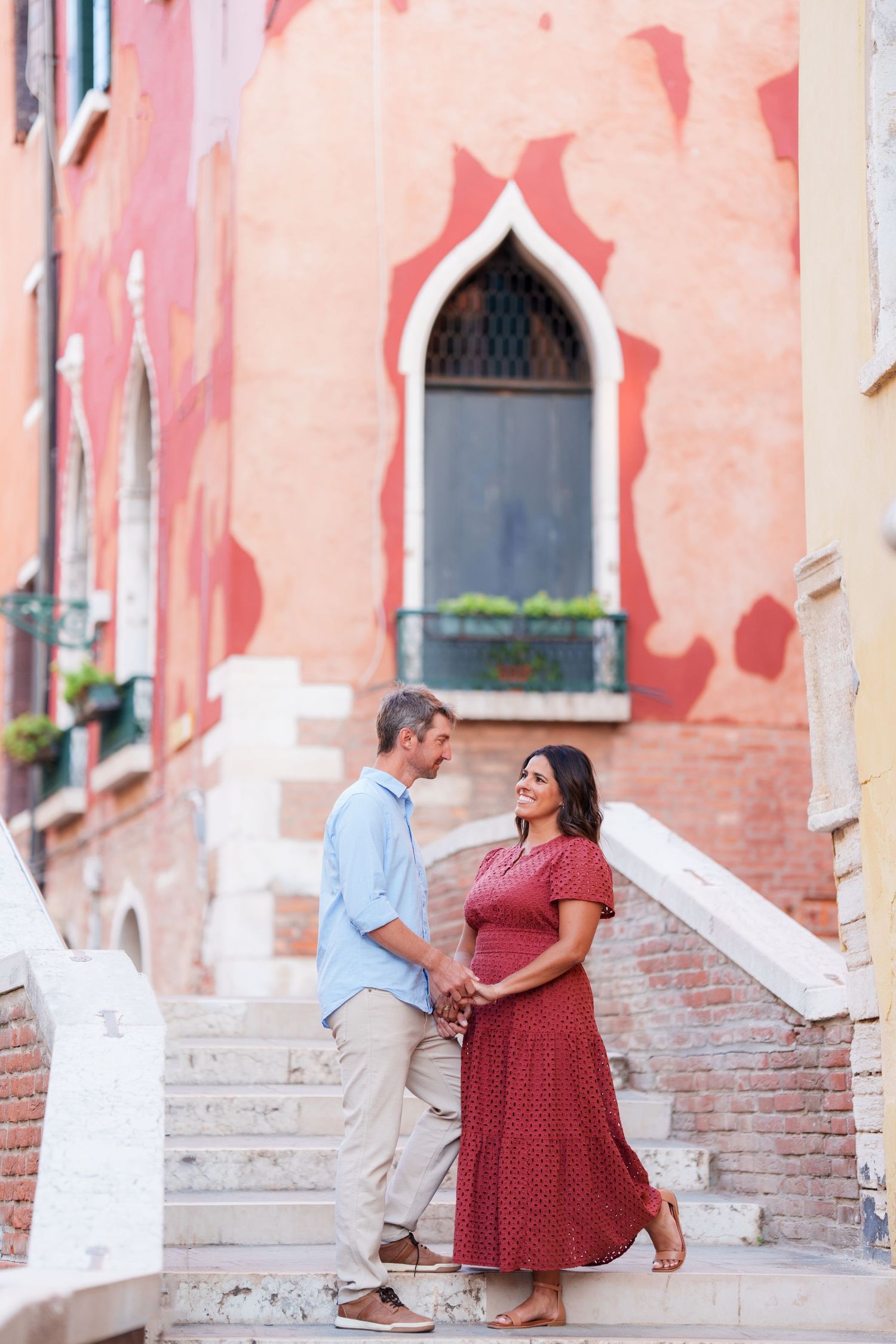 Romantic couple holding hands on stone steps in Venice, Italy, with colorful historic architecture in the background.