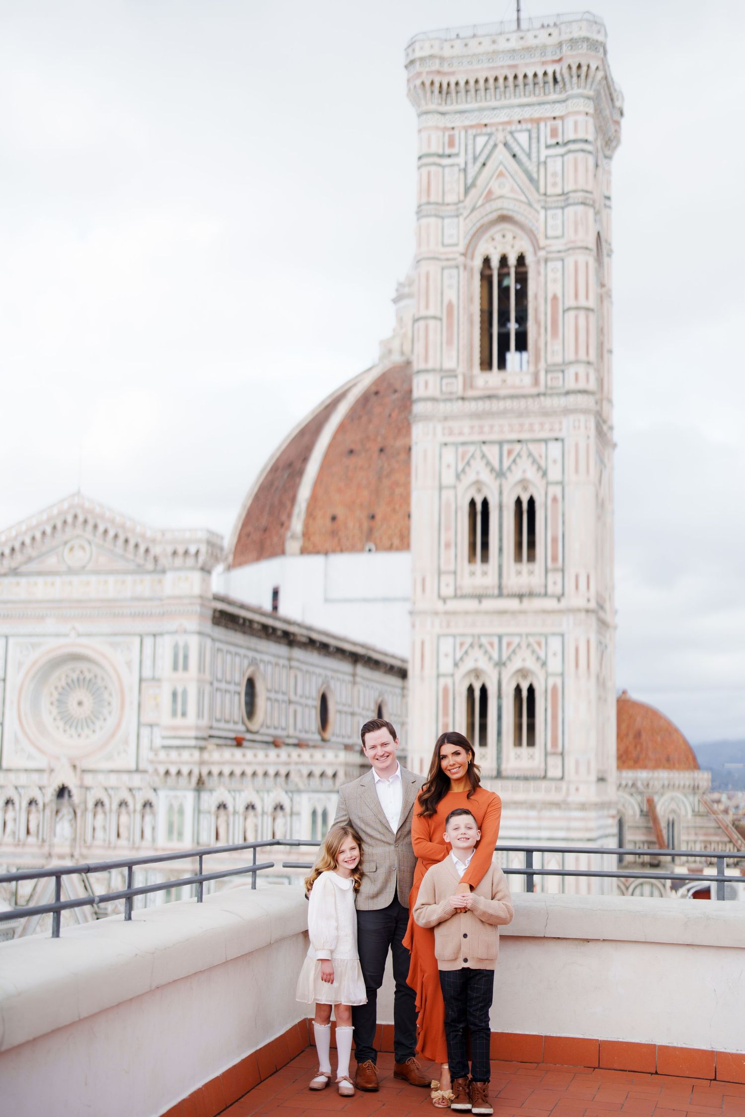 Family of four posing on a rooftop terrace with Florence Cathedral and Giotto's Campanile in the background.