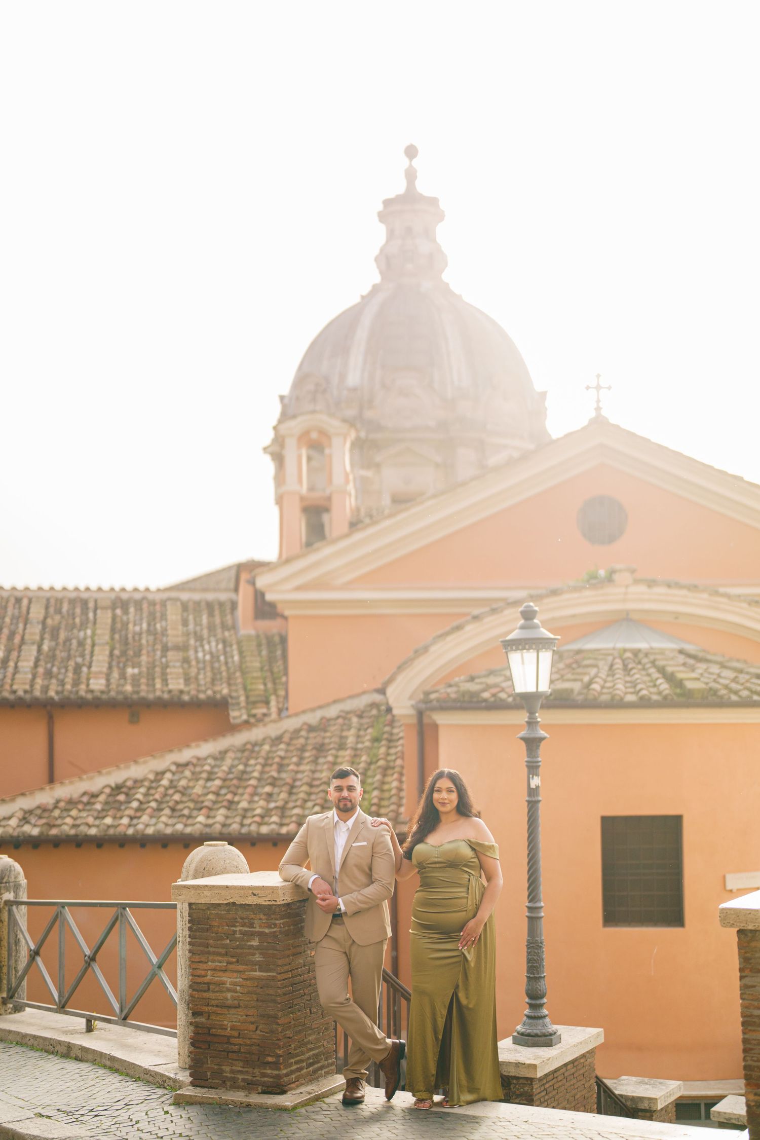 Couple posing on a Roman terrace with a baroque church dome and warm golden light in Rome, Italy.