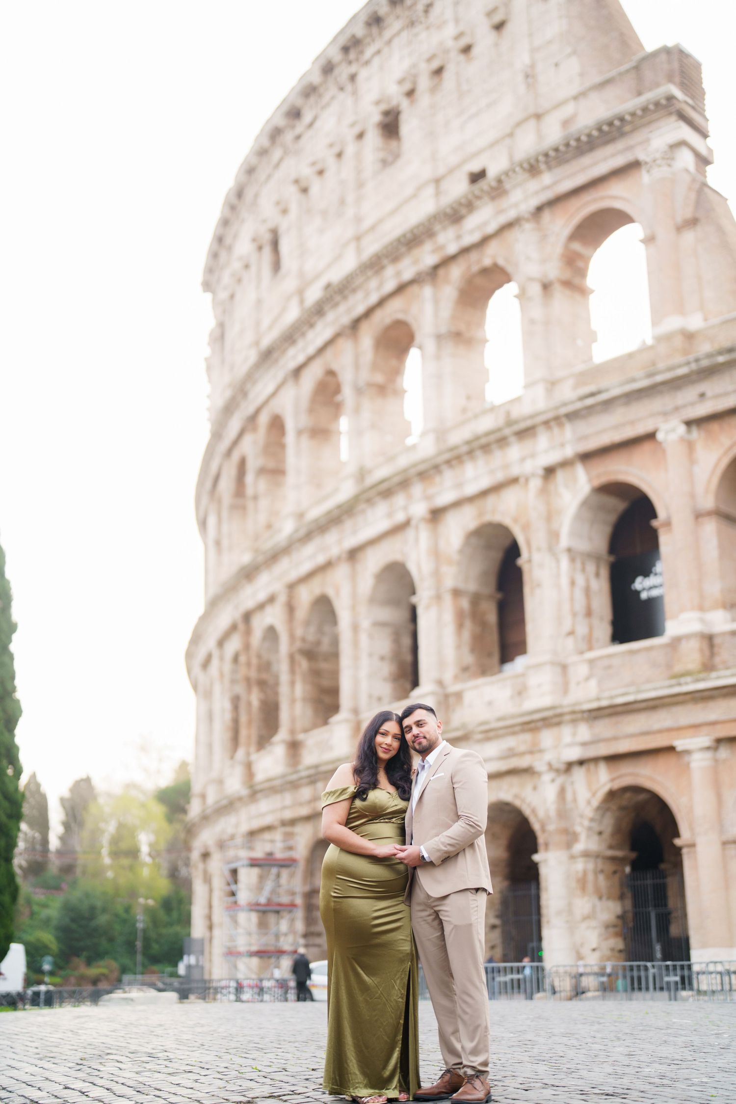 Couple posing in front of the Colosseum in Rome, woman in green maternity gown, man in beige suit.