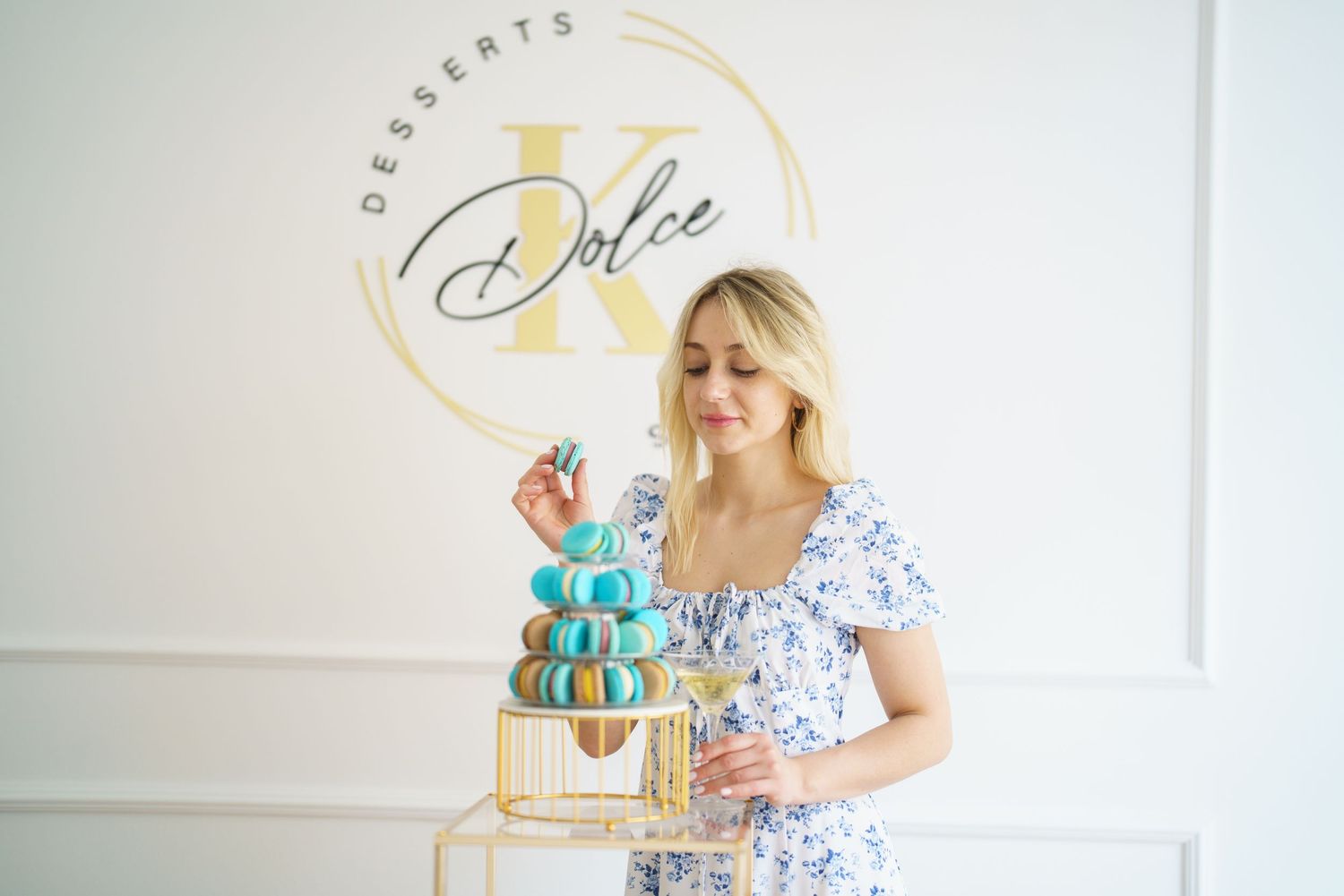 Woman arranging macarons on a gold tower stand at Dolce K Desserts bakery.