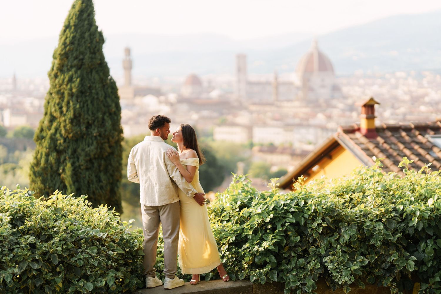 Romantic couple kissing on a terrace overlooking Florence skyline with Duomo cathedral and cypress trees in Italy.