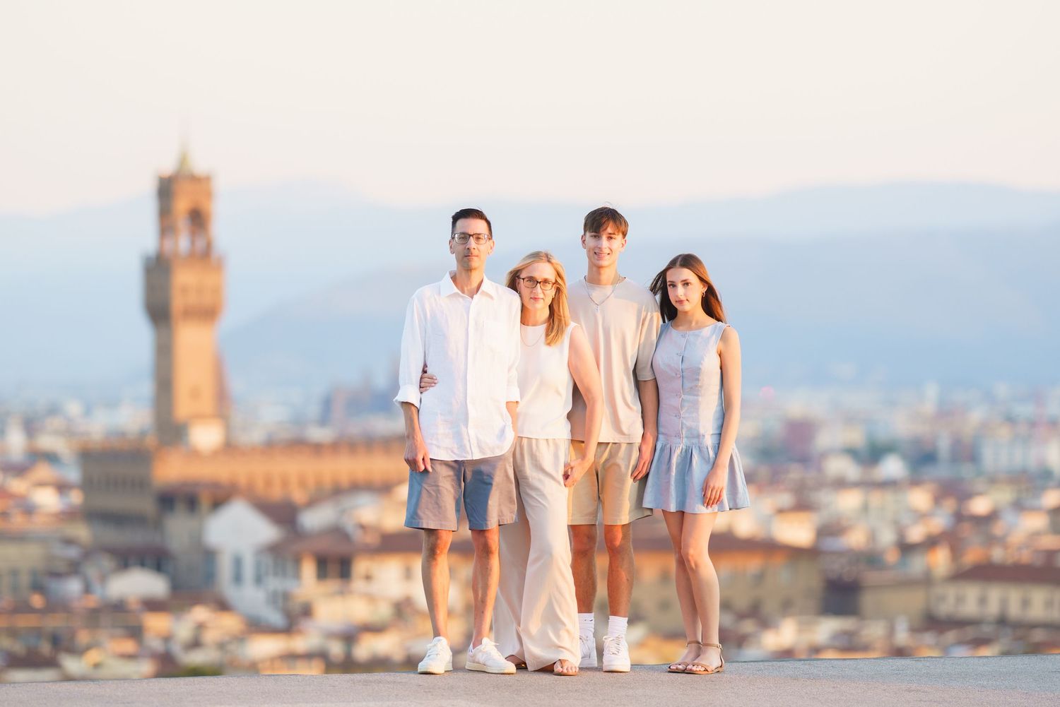 A family wearing white and blue outfits poses together against a coastal Mediterranean cityscape backdrop.