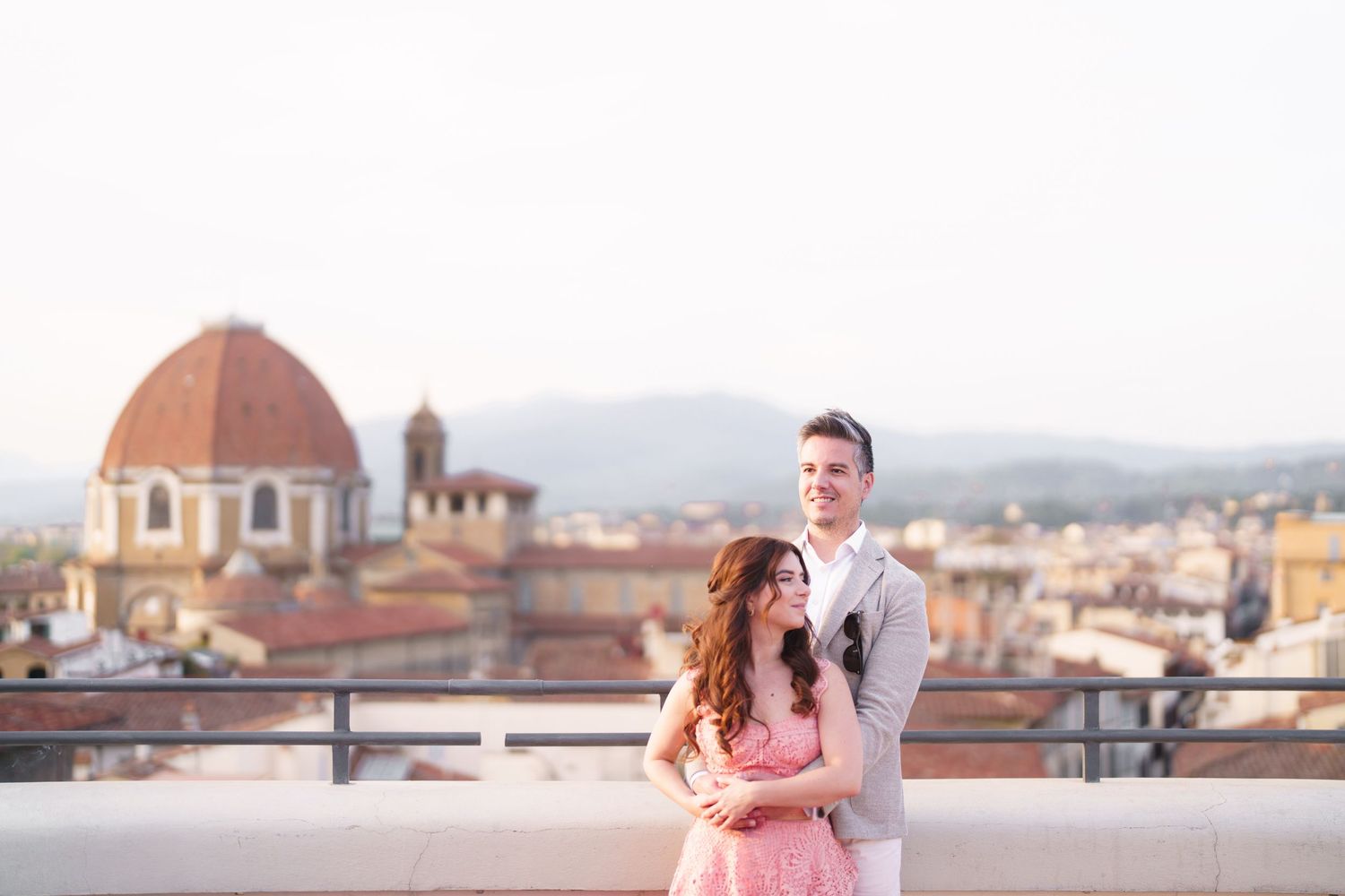 A couple embraces on a rooftop terrace overlooking the historic skyline of Florence, Italy with its iconic Duomo cathedral.