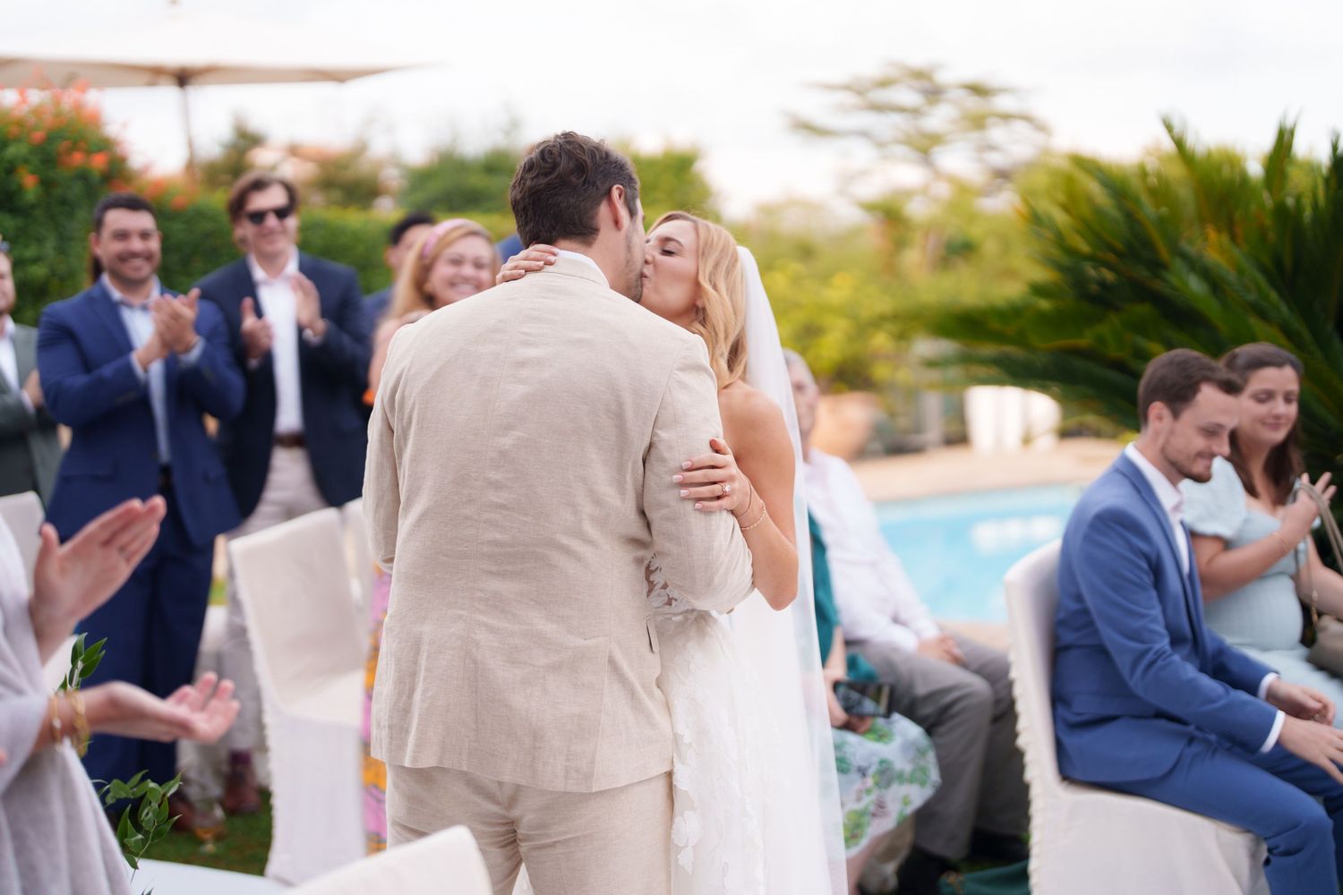 Outdoor wedding celebration with guests in formal attire near a swimming pool.
