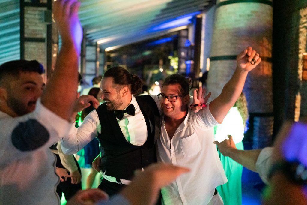 Party guests dancing under vibrant multicolored lights at a wedding reception.