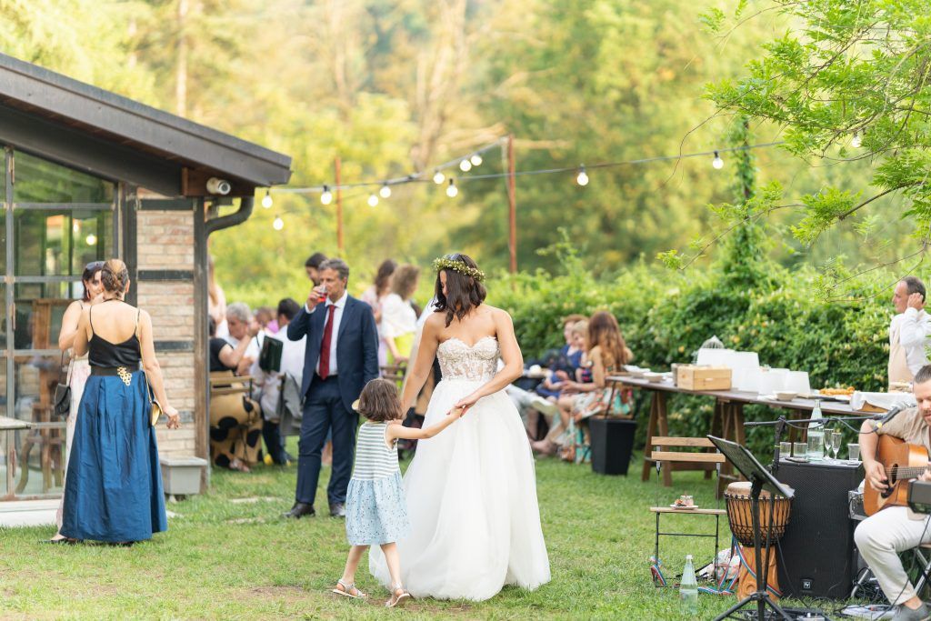 Wedding guests mingle and dance at an outdoor garden reception with string lights overhead.