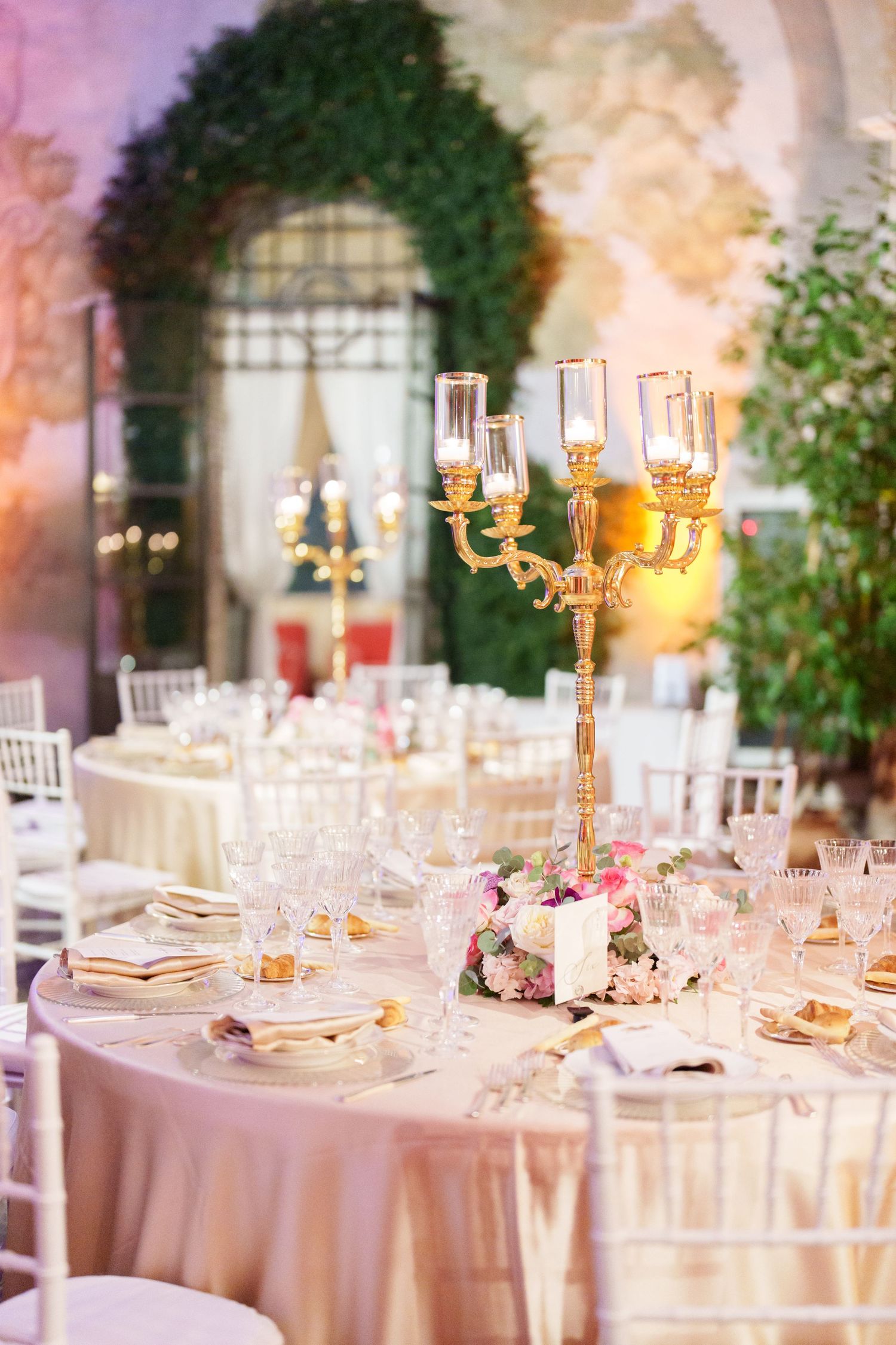 Luxurious wedding reception tables with gold candelabras and pink floral centerpieces.